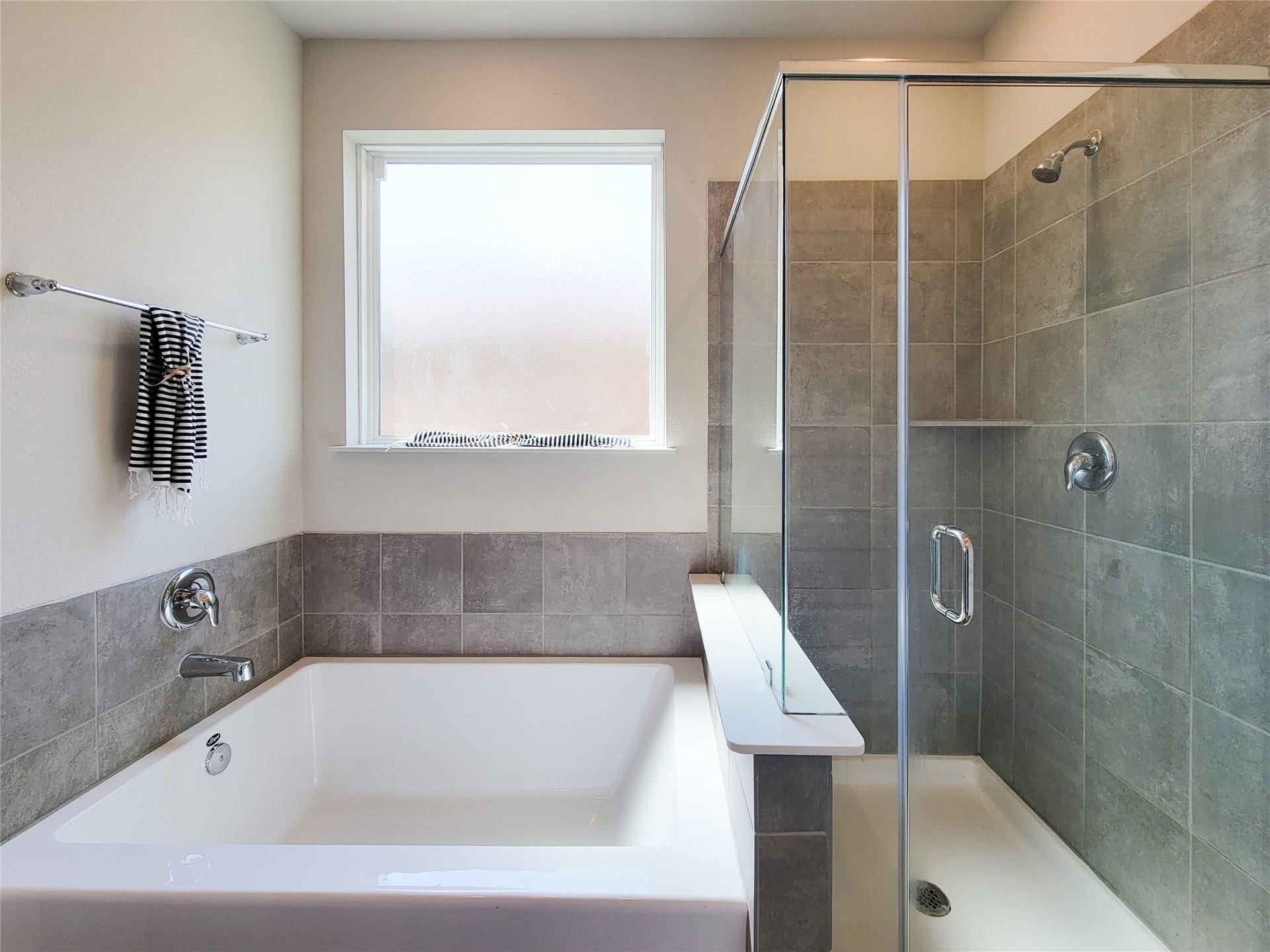 10843 Bodie Hills Drive, Rosharon, TX 77583 Luxurious bathroom featuring a large soaking tub and a sleek glass-enclosed shower, accented with elegant gray tiles.