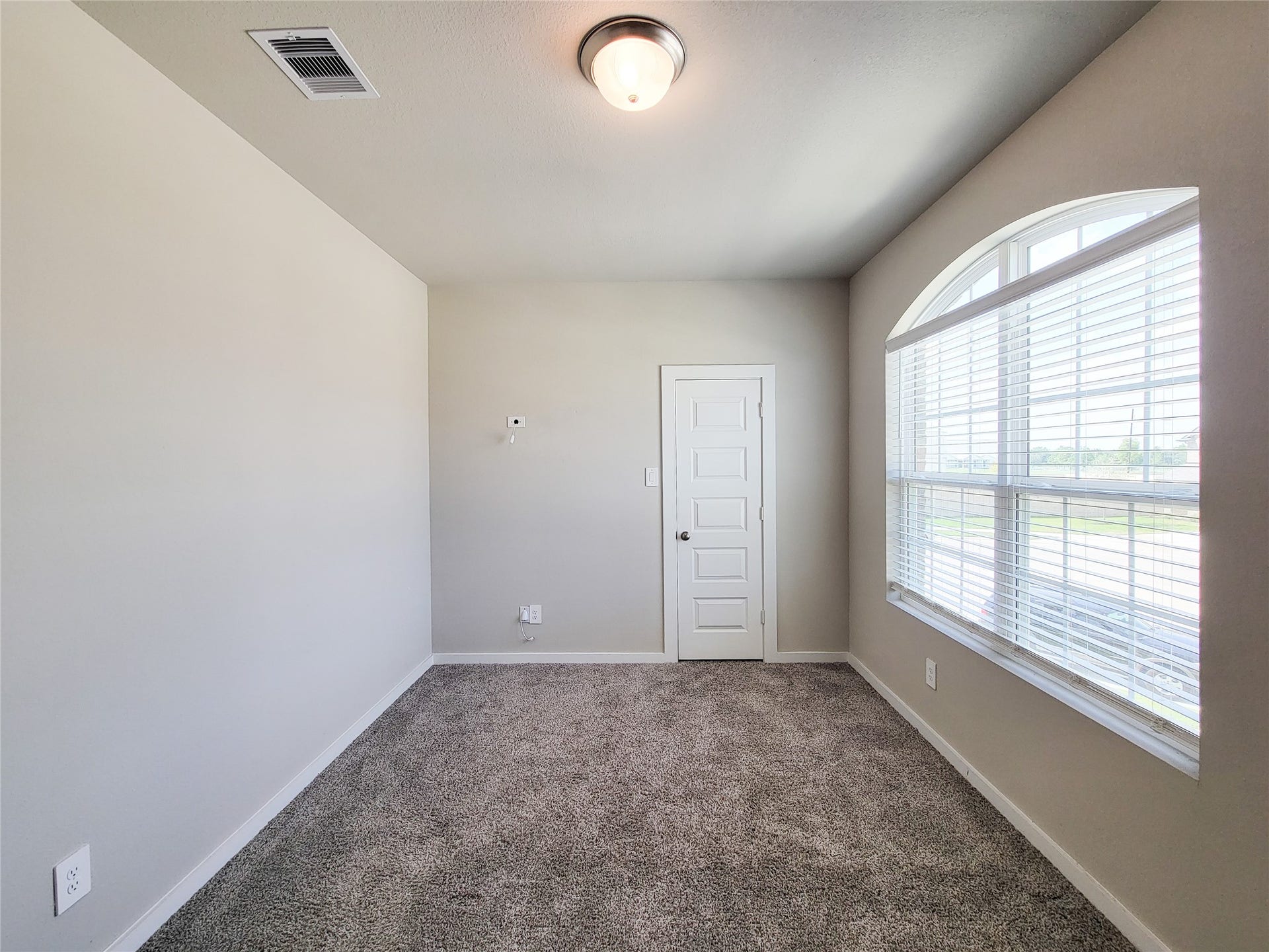 10843 Bodie Hills Drive, Rosharon, TX 77583 Bright and cozy room featuring plush carpeting, a large arched window for ample natural light, and a modern light fixture, perfect for a home office or guest bedroom.