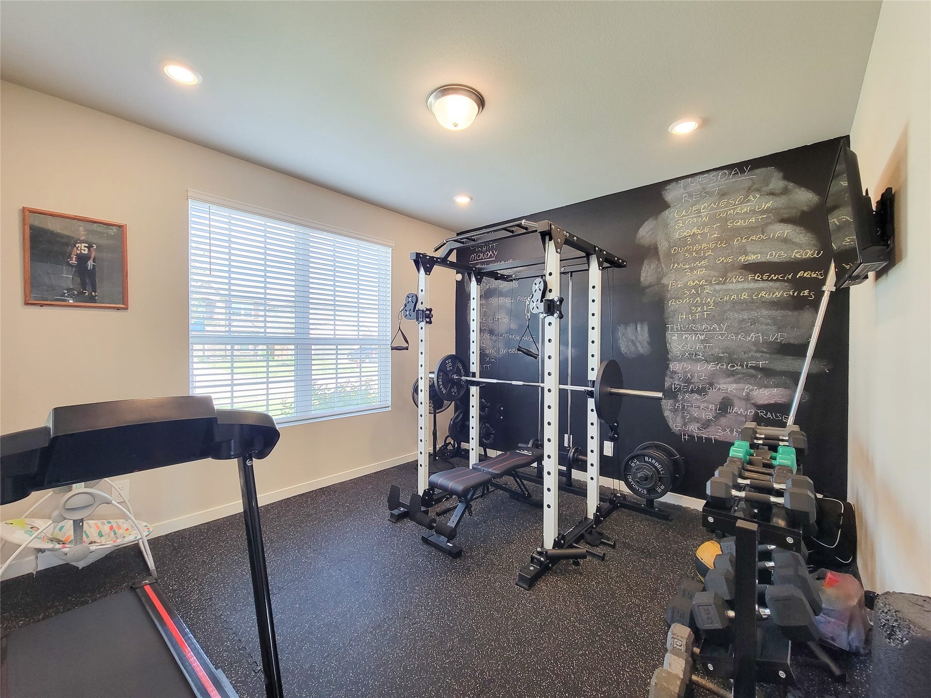 10843 Bodie Hills Drive, Rosharon, TX 77583 Bright and functional home gym featuring a versatile workout station, dumbbell rack, treadmill, and a motivational chalkboard wall.