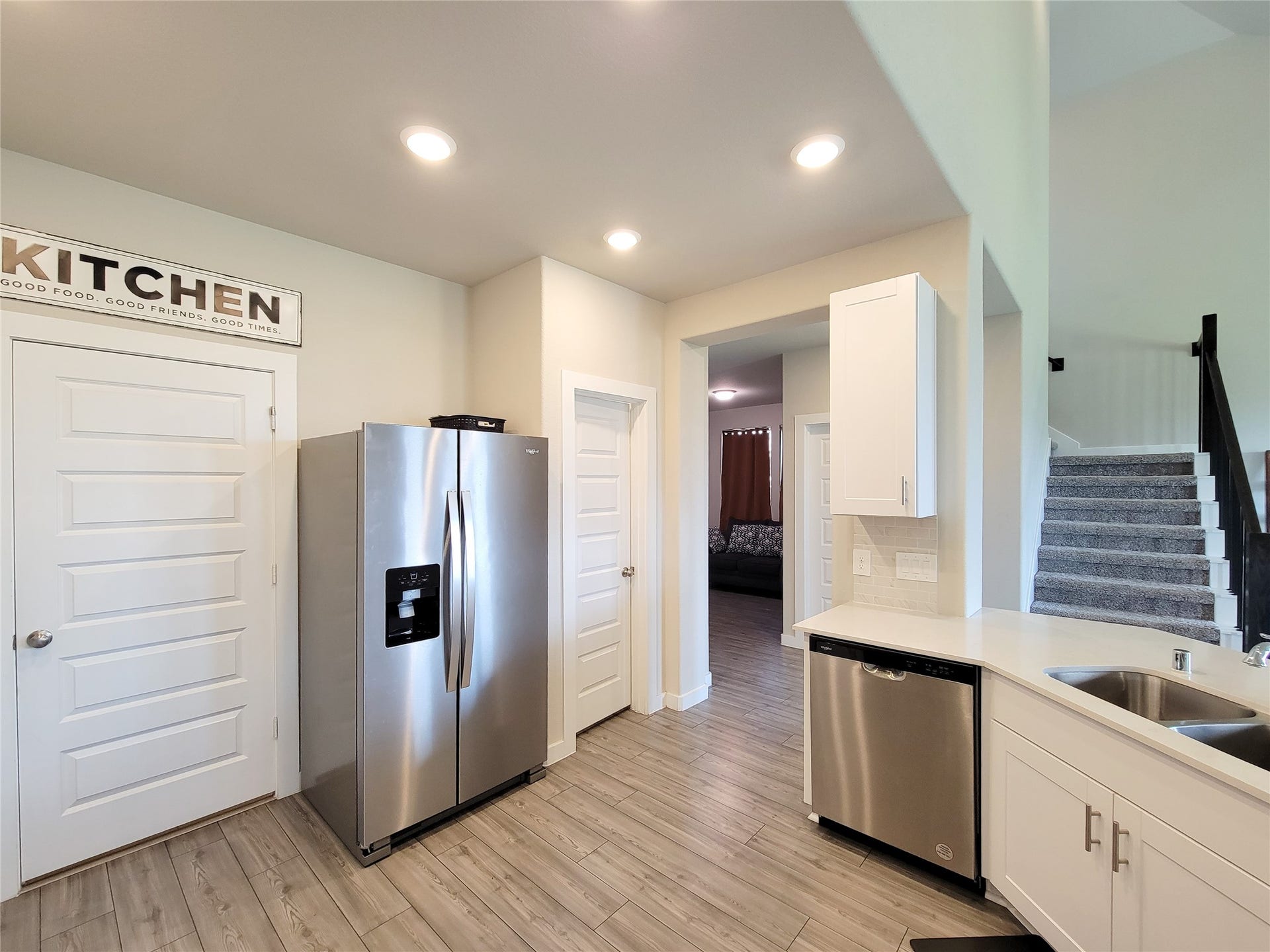10843 Bodie Hills Drive, Rosharon, TX 77583 Modern kitchen with stainless steel appliances, ample cabinetry, and sleek wood flooring, leading to a cozy living area and carpeted staircase.