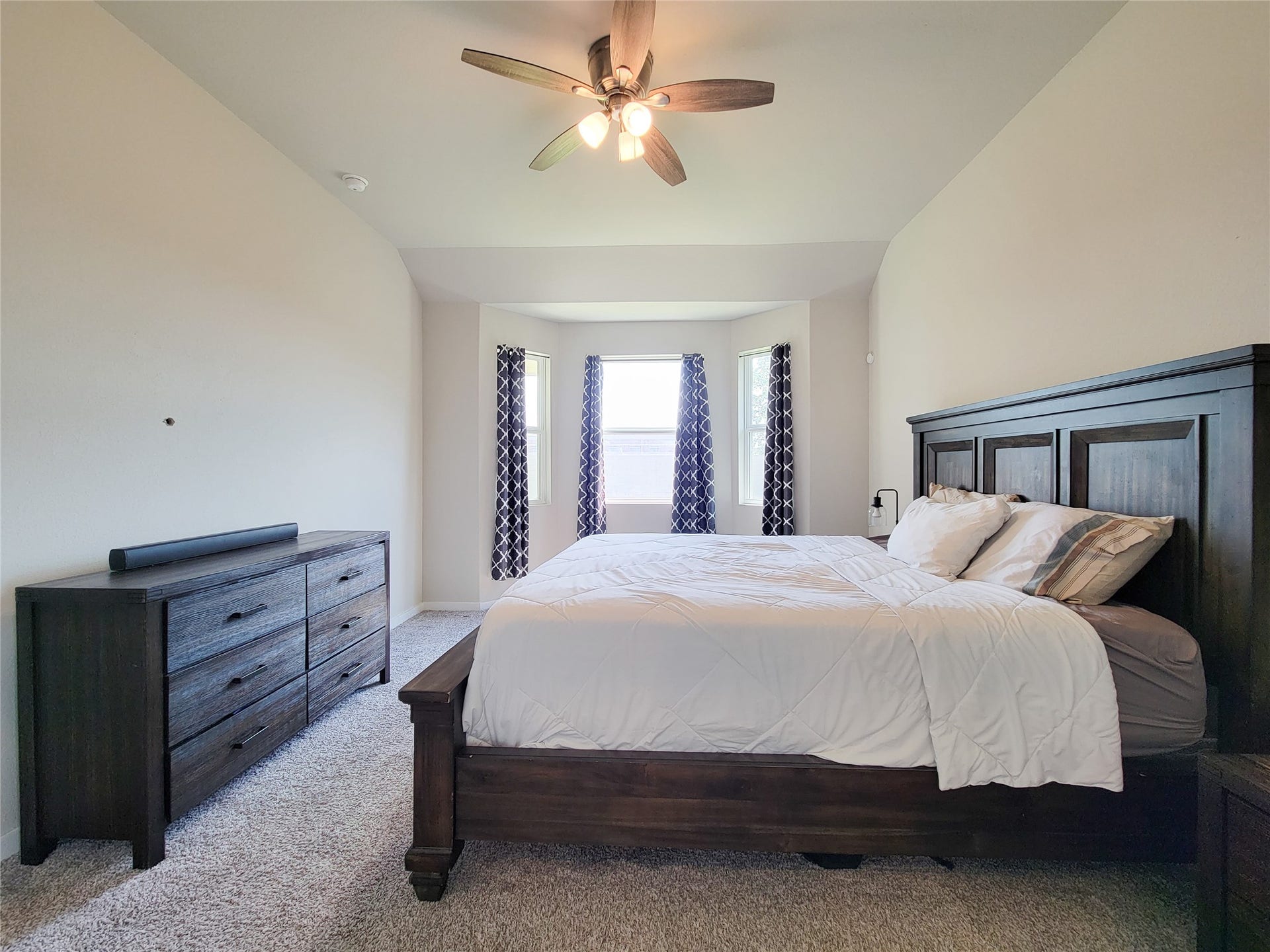 10843 Bodie Hills Drive, Rosharon, TX 77583 Spacious bedroom with a cozy bay window, elegant dark wood furniture, and soft carpeting, complemented by a modern ceiling fan for comfort.