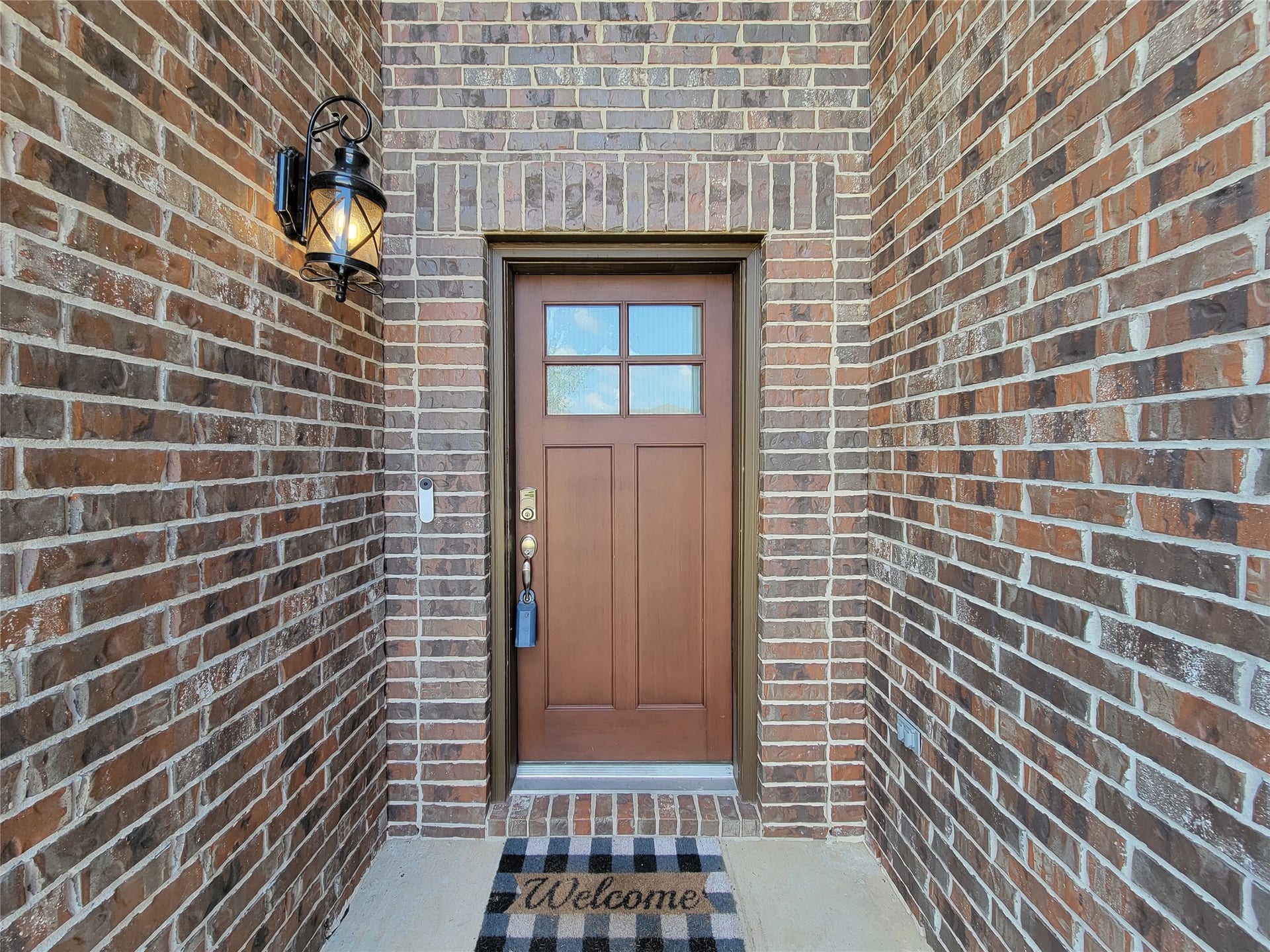 10843 Bodie Hills Drive, Rosharon, TX 77583 Charming brick entryway with a classic wooden door and a welcoming lantern sconce, complemented by a cozy doormat.