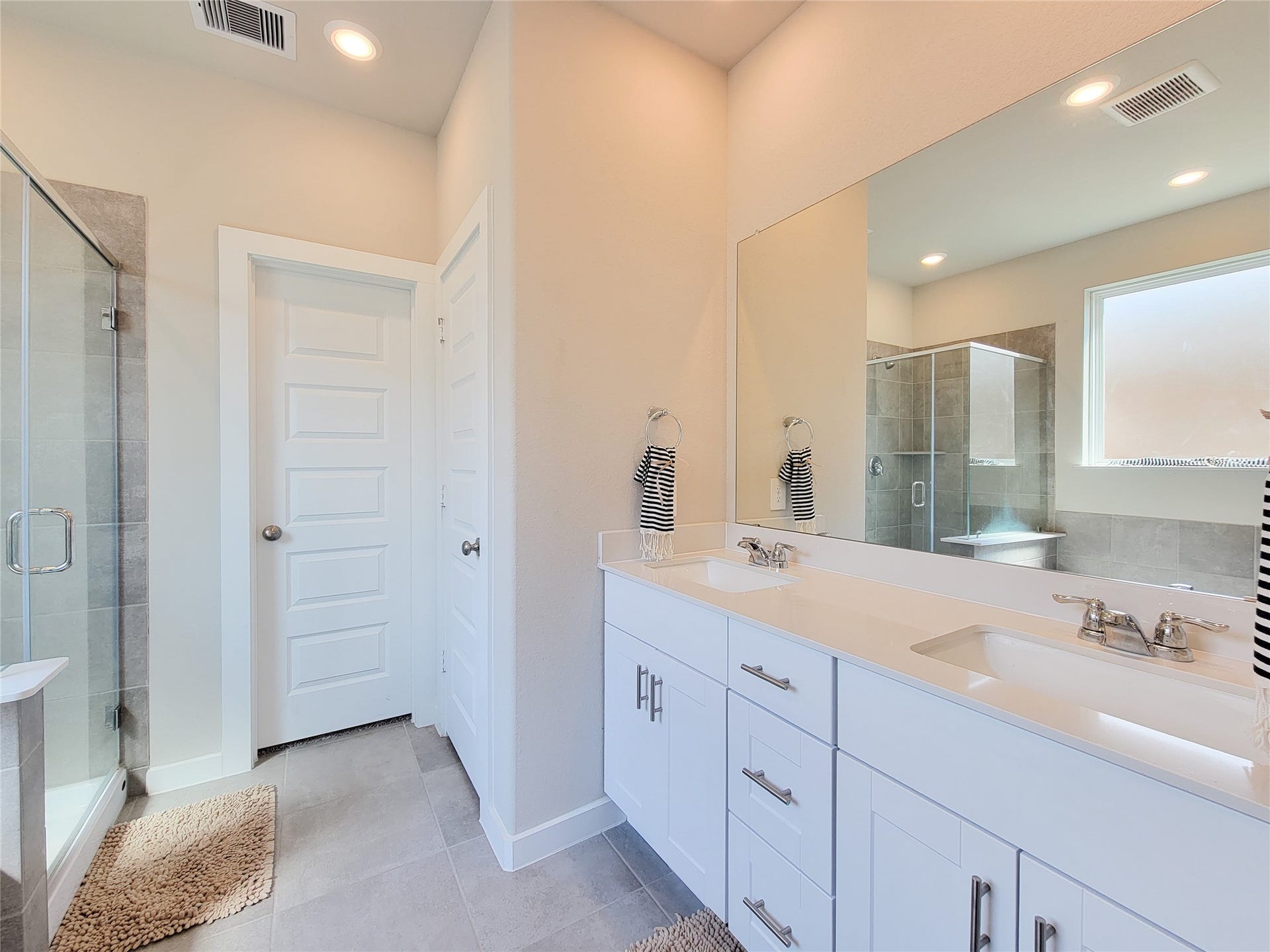 10843 Bodie Hills Drive, Rosharon, TX 77583 Bright and modern bathroom featuring double sinks, a large mirror, and a spacious glass-enclosed shower, complemented by elegant fixtures and neutral tile flooring.