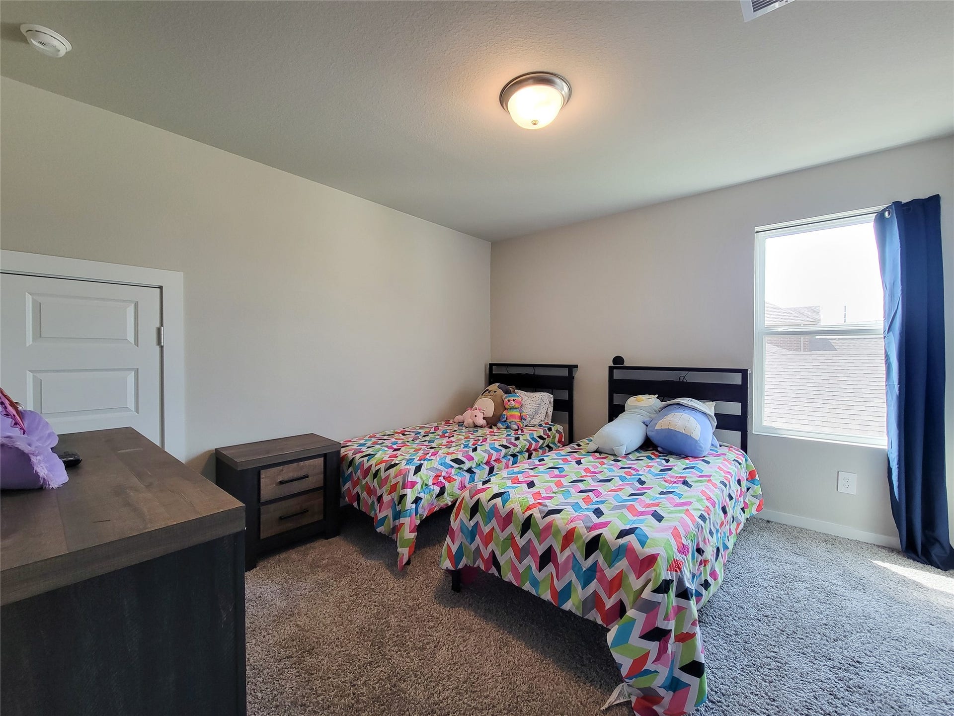 10843 Bodie Hills Drive, Rosharon, TX 77583 Cozy bedroom featuring twin beds with colorful bedding, plush carpet, and ample natural light from a large window, creating a warm and inviting atmosphere.