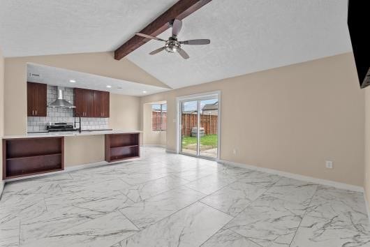 11007 Green Arbor Drive, Houston, TX 77089 This spacious living area features a vaulted ceiling with an exposed beam and a ceiling fan. It has large marble-patterned tiles, with an open concept to the kitchen .with Sliding glass doors provide access to a fenced backyard, offering plenty of natural light.