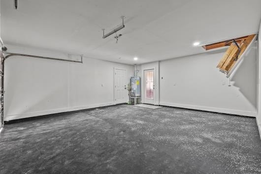 11007 Green Arbor Drive, Houston, TX 77089 This photo shows a spacious, clean garage with a concrete floor, white walls, and ceiling. It features a water heater, access to the attic via a pull-down ladder, and a door leading outside. The space is well-lit with overhead lighting.