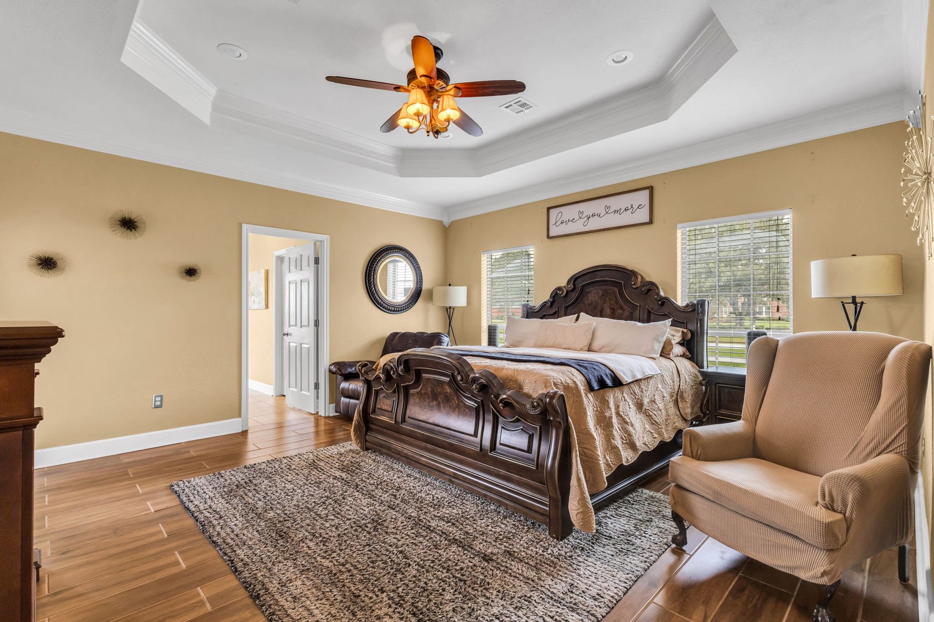 11010 Madison Court, Beaumont, TX 77705 Spacious primary bedroom featuring a tray ceiling with crown molding, wood-look tile flooring, and large windows that bring in natural light. Plenty of room for additional furnishings and a comfortable sitting area.