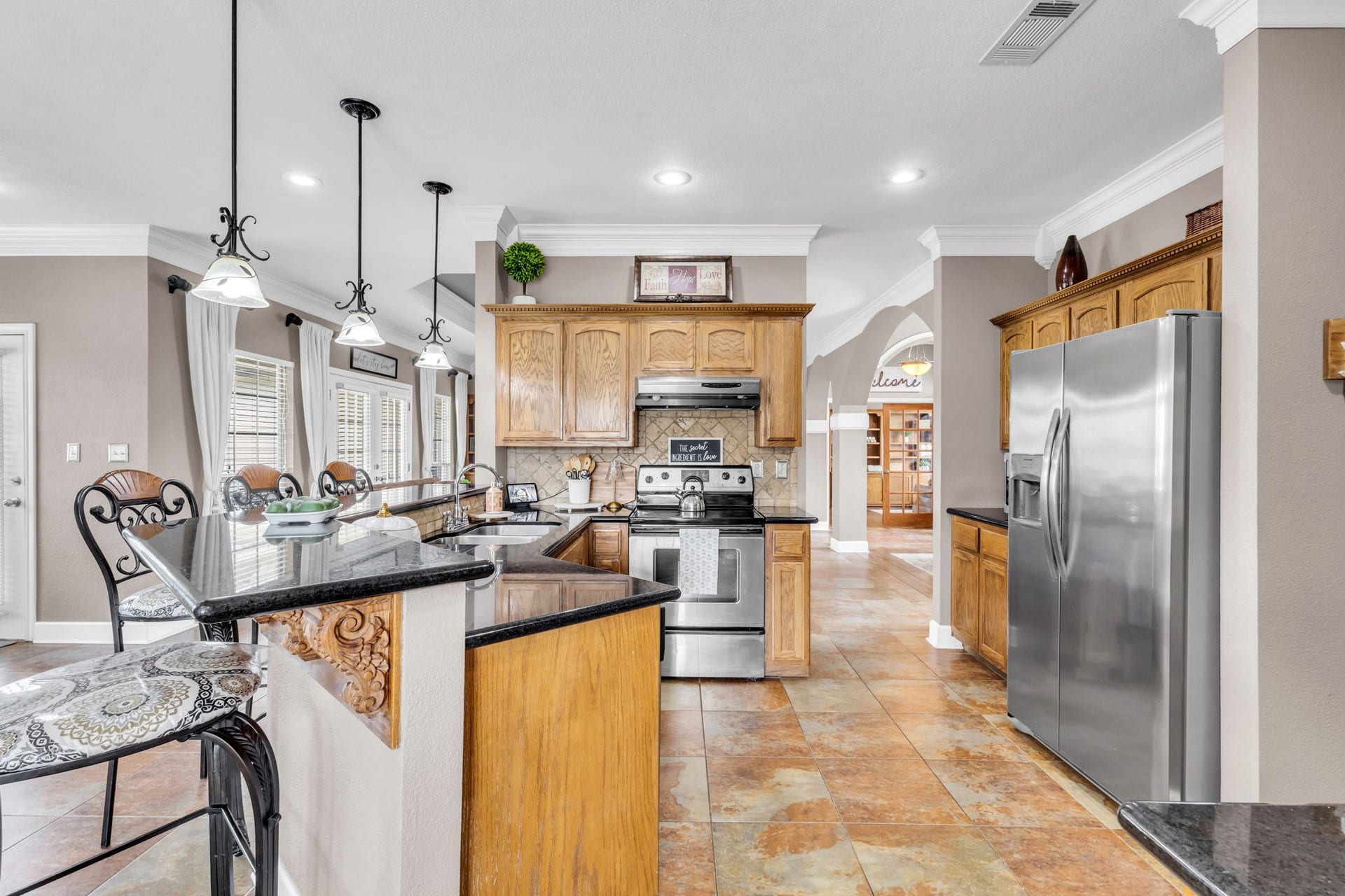 11010 Madison Court, Beaumont, TX 77705 Additional kitchen view showcasing expansive dark countertops, rich wood cabinetry, decorative tile backsplash, and a functional layout with generous counter space. Recessed lighting and crown molding add a polished touch to this inviting space.