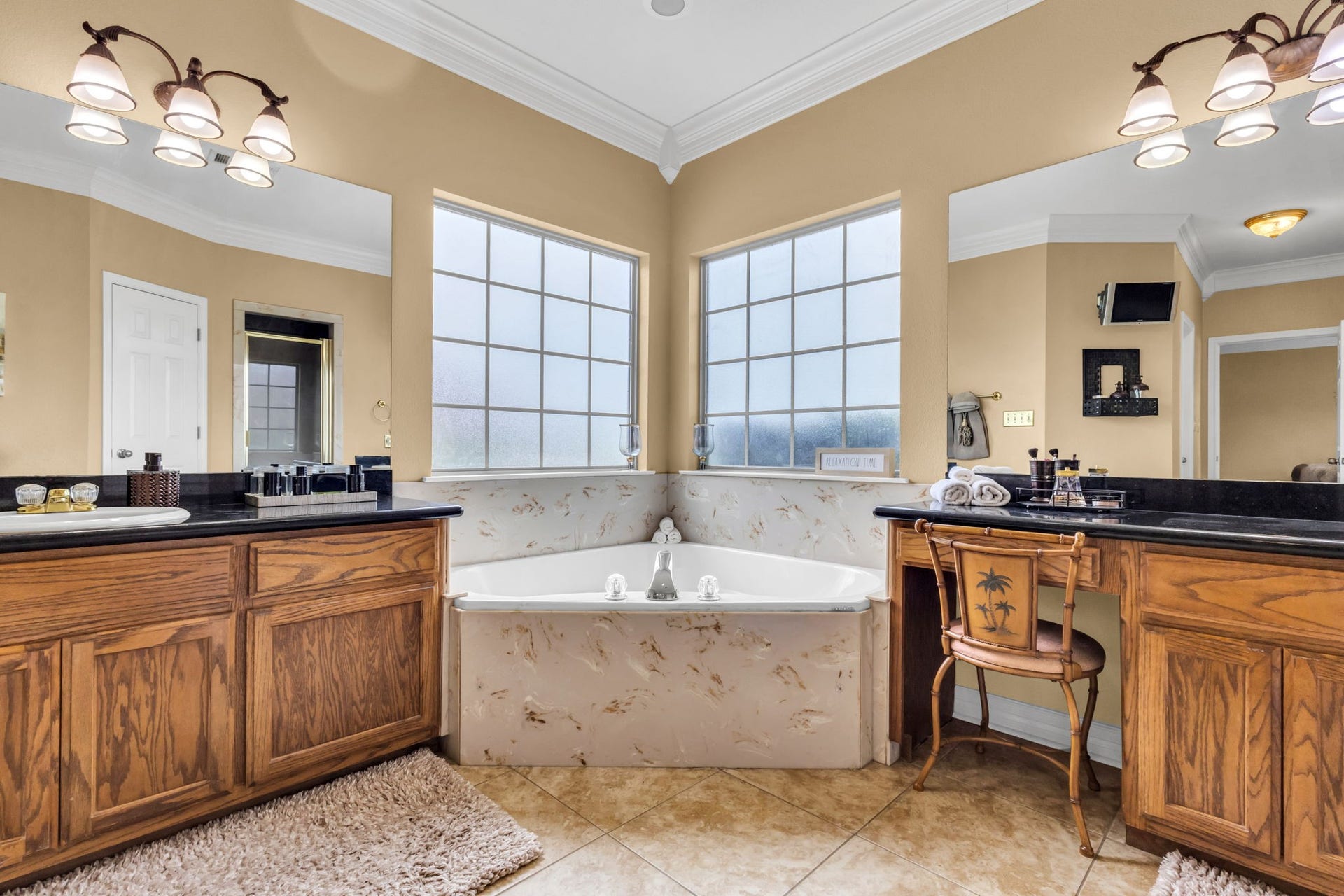 11010 Madison Court, Beaumont, TX 77705 Another view of the spacious primary bathroom highlights the corner soaking tub beneath two large windows, separate vanities with dark countertops, and generous cabinet storage.