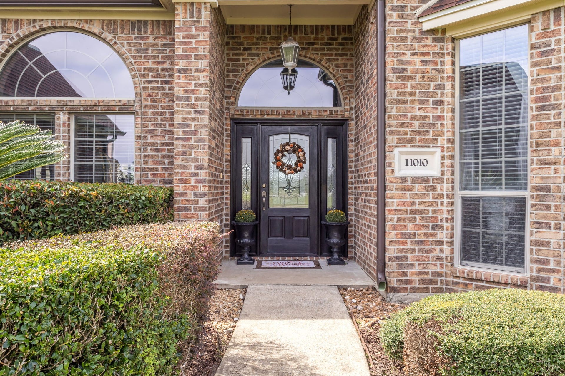 11010 Madison Court, Beaumont, TX 77705 Welcoming covered front entry featuring an elegant glass-paneled door with decorative sidelights, arched windows, and beautifully maintained landscaping.