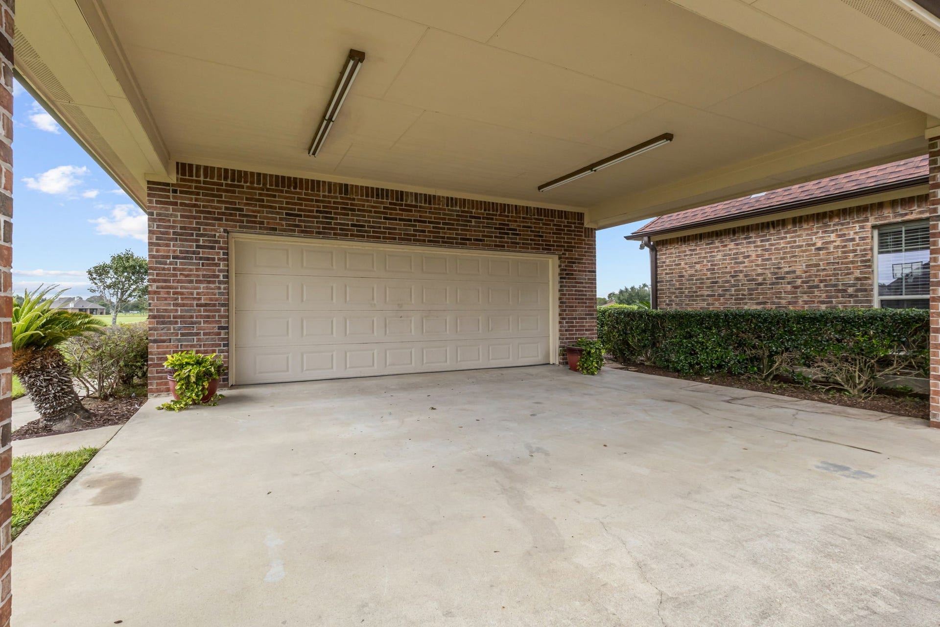11010 Madison Court, Beaumont, TX 77705 Spacious detached two-car garage with an expansive covered concrete carport parking area, overhead lighting, and convenient access. The brick exterior and surrounding landscaping complement the home's overall appeal.