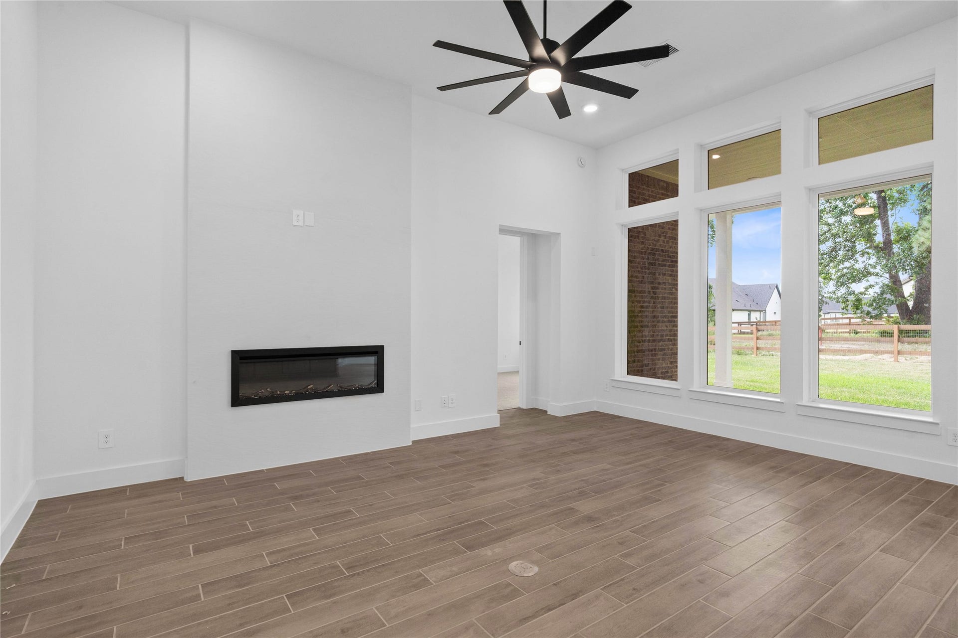 17728 Gold Saddle Lane, Magnolia, TX 77354 Spacious and light-filled living area showcasing an open layout, neutral tones, and wide plank tile flooring that enhances the airy feel. Large windows invite natural light and gorgeous views of the backyard green space.