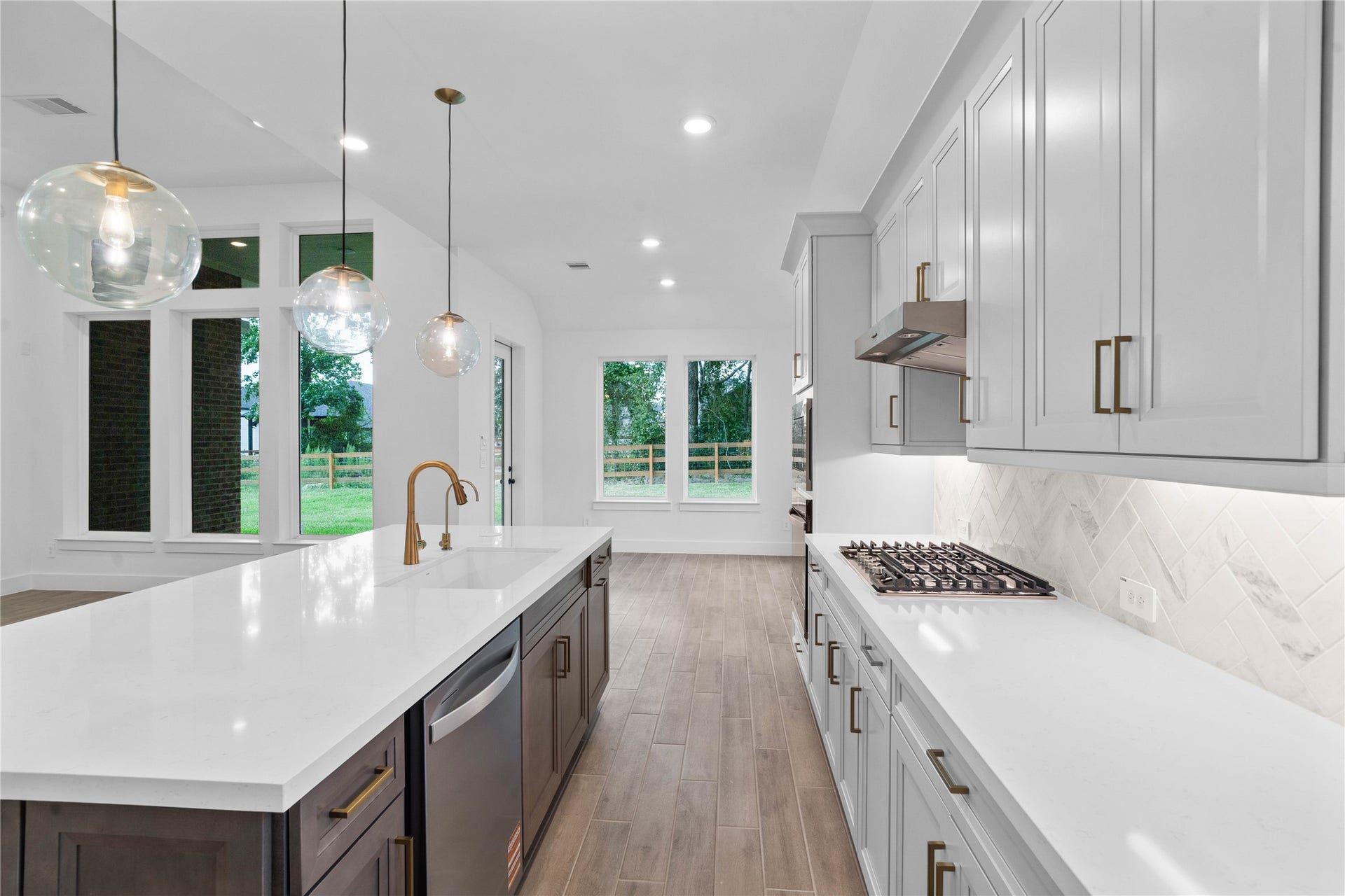 17728 Gold Saddle Lane, Magnolia, TX 77354 This kitchen features sleek light gray cabinetry, pristine white quartz countertops, and a tile backsplash, creating a clean and contemporary aesthetic. Equipped with stainless steel appliances including a built-in oven, microwave, gas stove top, modern range hood, and dishwasher - space offers both style and functionality.