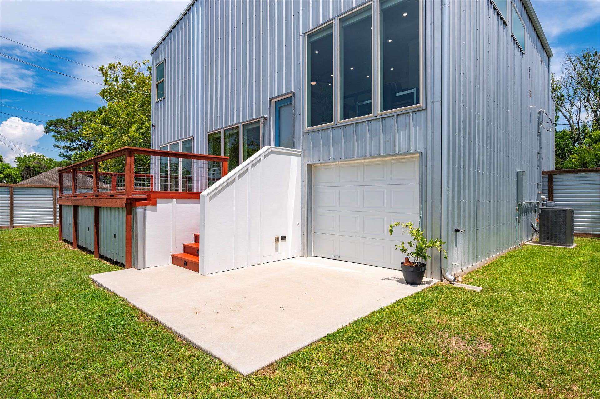 13149 W 6th Street, Santa Fe, TX 77510 Back of the home with raised decking, accent lights and back door to pass-thru garage. Exterior walls made from 26 gauge galvalume R-panel steel in silver and blue.