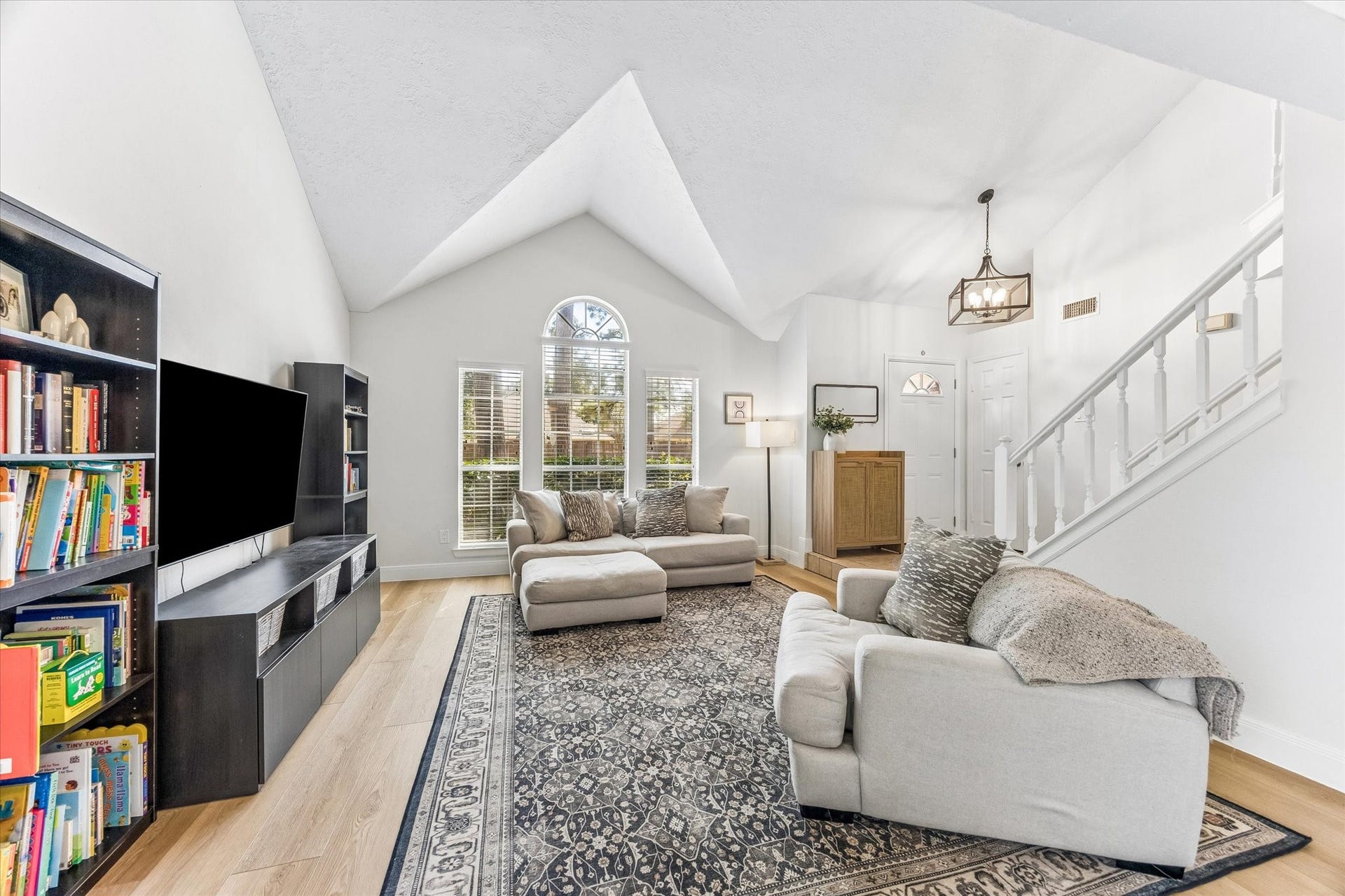 1043 Danforth Drive, Houston, TX 77062 Bright and inviting living room with vaulted ceilings, featuring cozy seating, a modern chandelier, and abundant natural light from large windows.