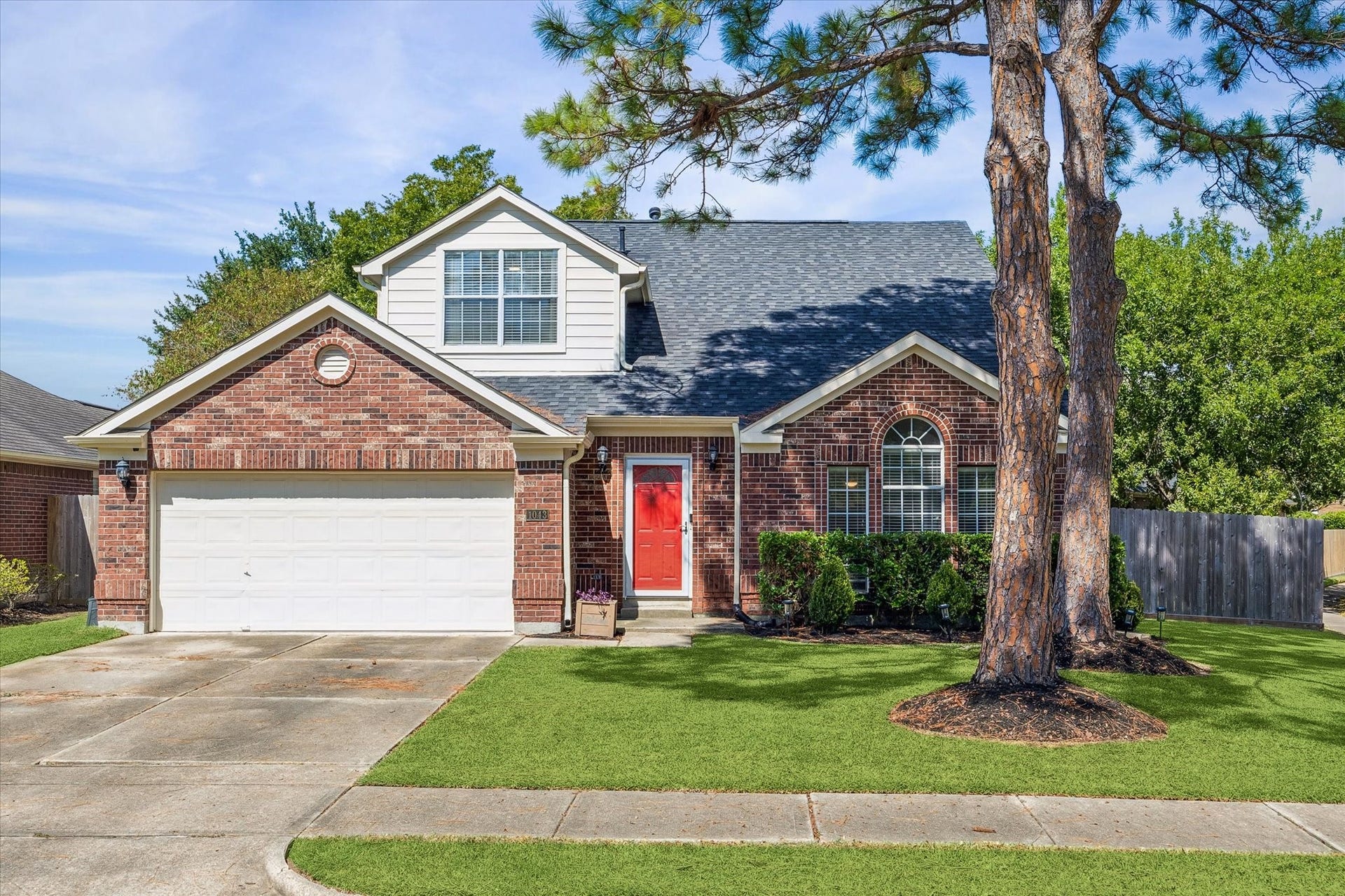 1043 Danforth Drive, Houston, TX 77062 Charming brick home featuring a bright red front door, lush green lawn, and a large tree providing shade and character.