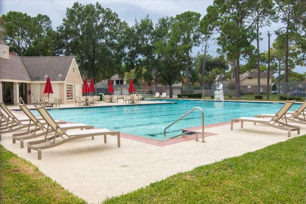 1043 Danforth Drive, Houston, TX 77062 Enjoy resort-style living with a spacious pool area, surrounded by lush greenery and equipped with comfortable loungers and vibrant red umbrellas for the perfect relaxation spot.
