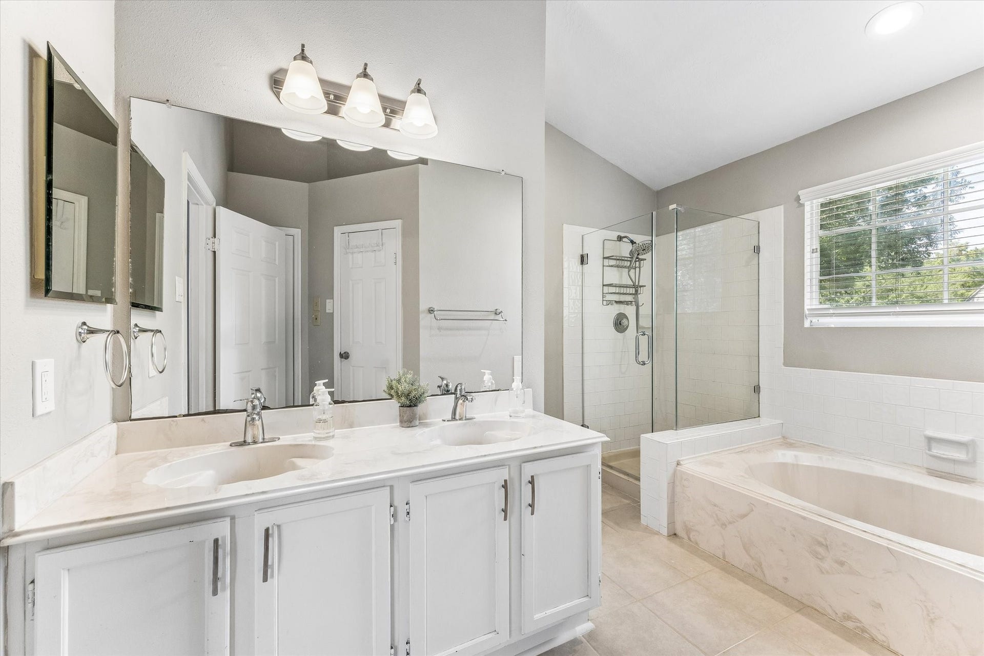 1043 Danforth Drive, Houston, TX 77062 Elegant 8x12 primary bathroom featuring a dual-sink vanity, a spacious glass-enclosed shower, and a luxurious soaking tub, all enhanced by natural light from a large window.