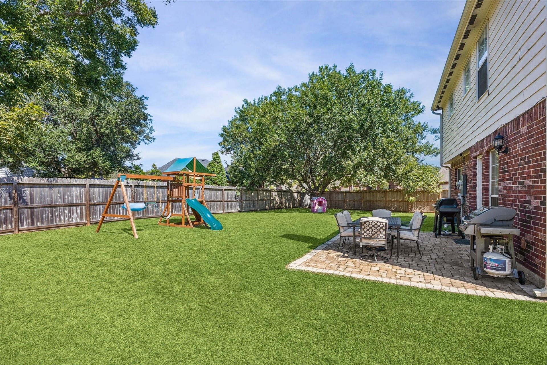 1043 Danforth Drive, Houston, TX 77062 Expansive backyard featuring a playset, lush lawn, and a cozy patio with outdoor dining and grilling area, perfect for family fun and entertaining.