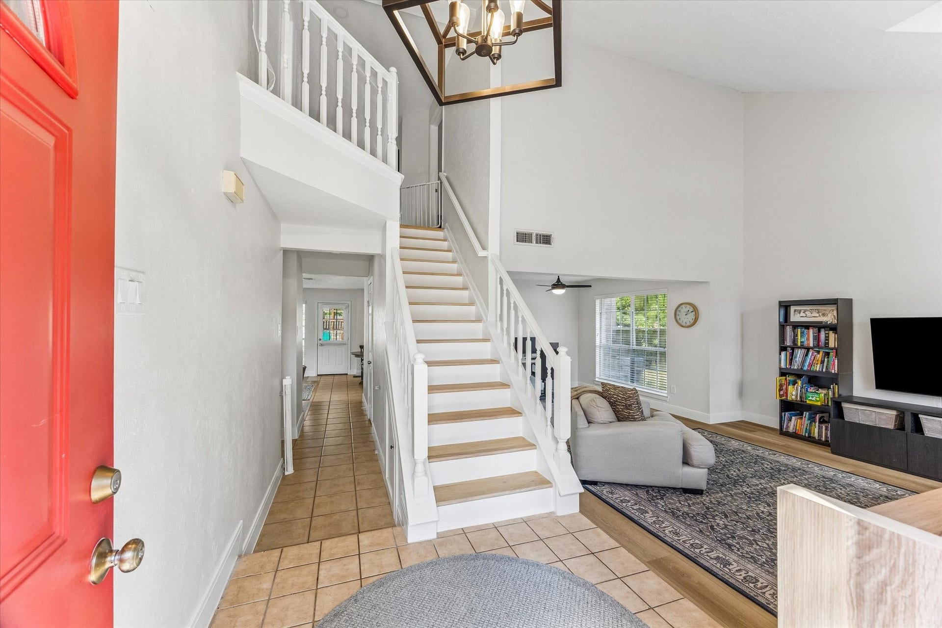 1043 Danforth Drive, Houston, TX 77062 Inviting entryway with a striking red door leads to a spacious, open-concept living area featuring high ceilings and a bright, airy atmosphere. The elegant staircase and cozy living room with a large window add charm and functionality.