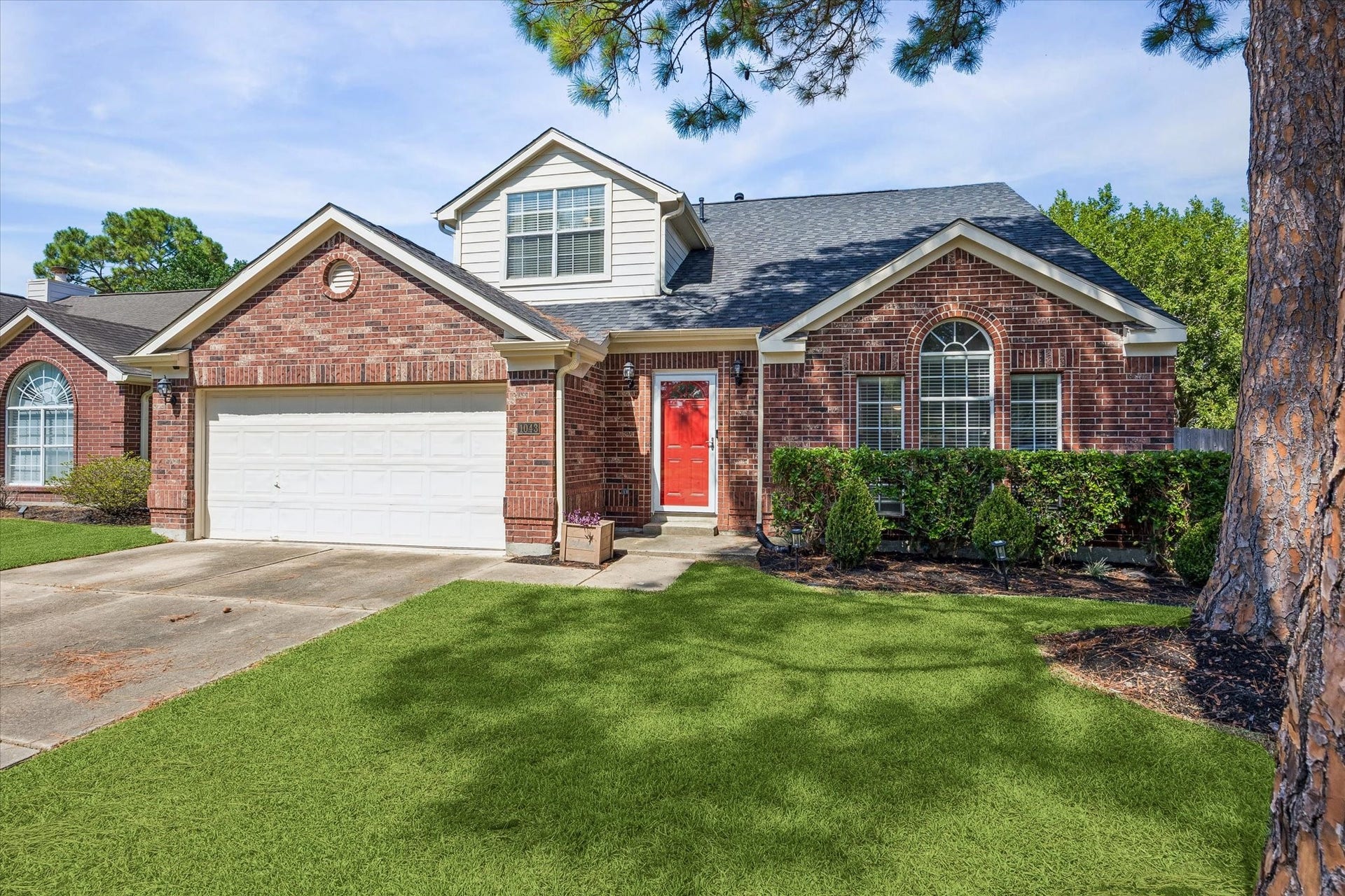 1043 Danforth Drive, Houston, TX 77062 Charming brick home with a striking red door, two-car garage, and beautifully manicured lawn, nestled in a serene neighborhood.