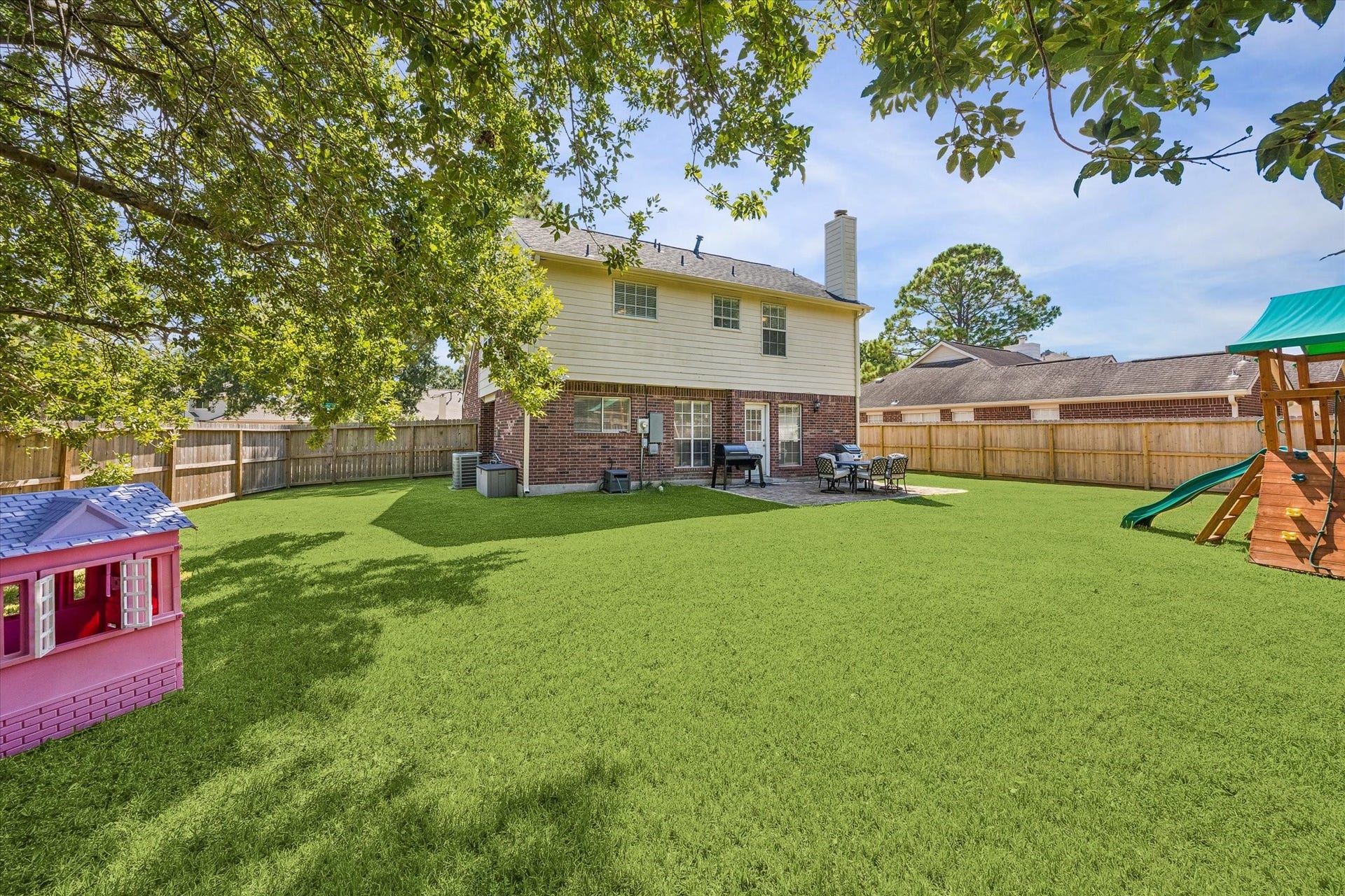 1043 Danforth Drive, Houston, TX 77062 Spacious backyard with lush green lawn, perfect for family gatherings, featuring a charming playhouse and playset, all set against a two-story brick home with a cozy patio area.