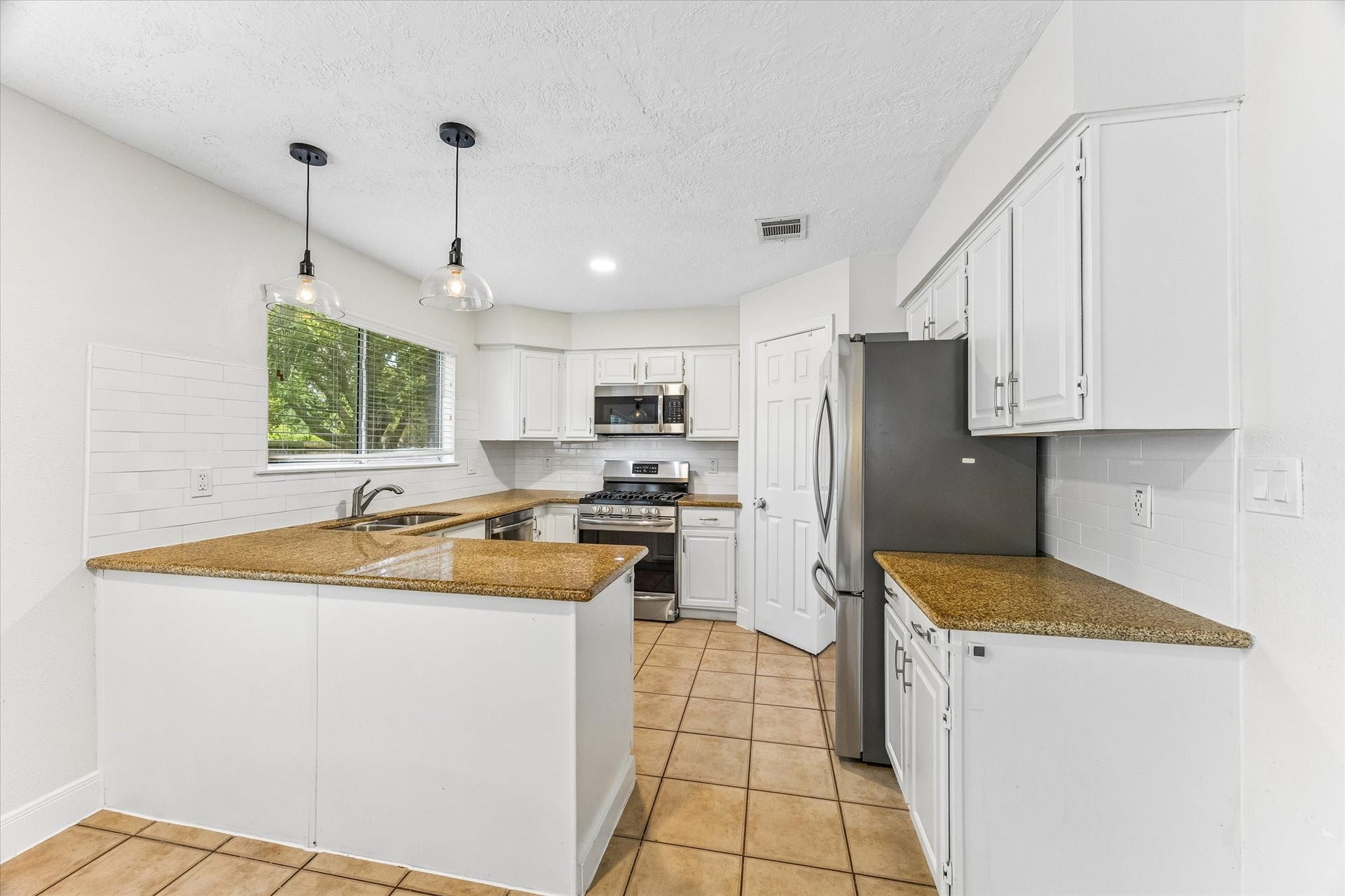 1043 Danforth Drive, Houston, TX 77062 Bright and inviting kitchen featuring white cabinetry, sleek stainless steel appliances, and warm tile flooring, enhanced by modern pendant lighting.