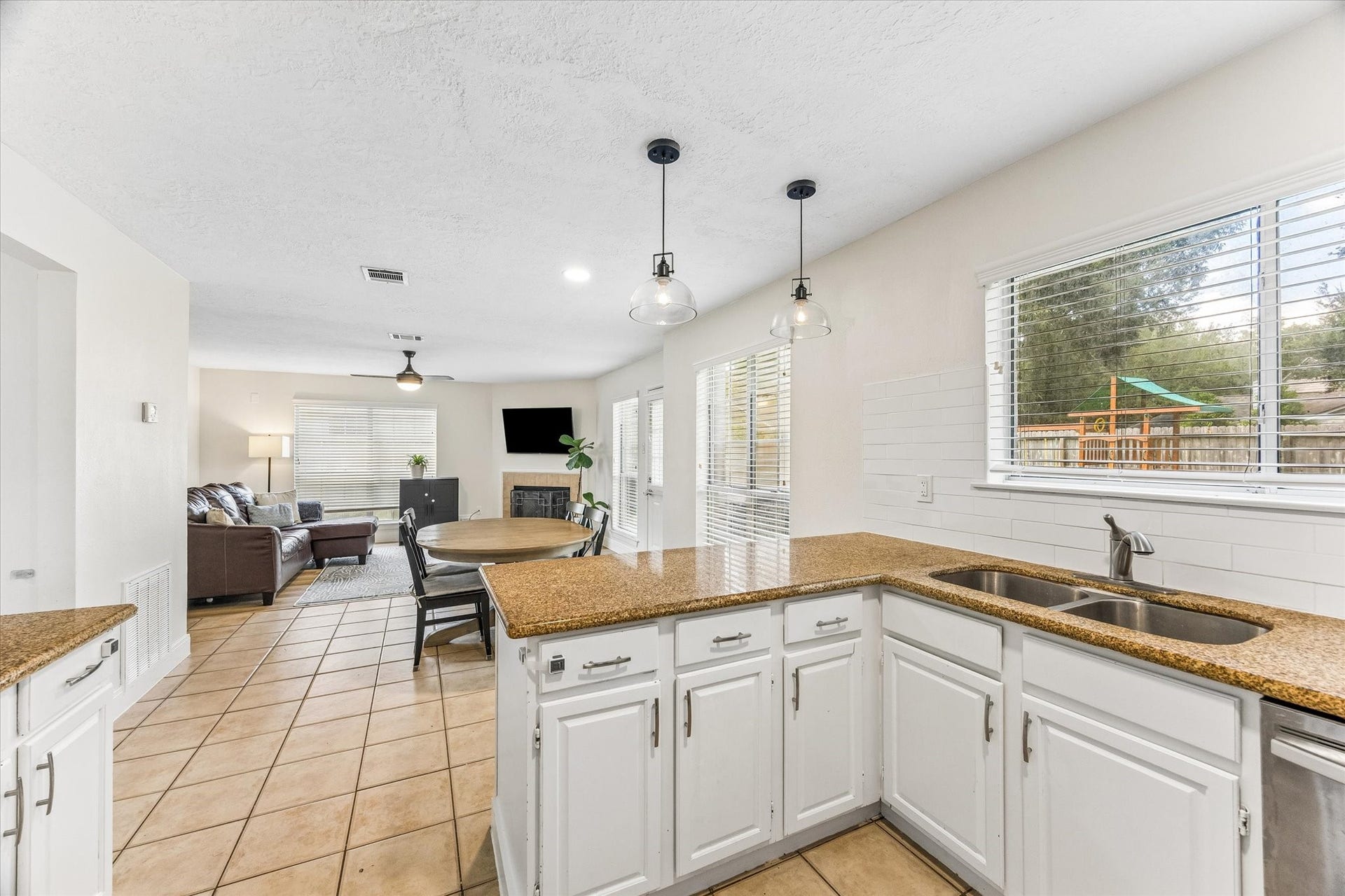 1043 Danforth Drive, Houston, TX 77062 Bright and open kitchen flows into a cozy living area with a fireplace, featuring tile flooring and ample natural light from large windows overlooking the backyard.