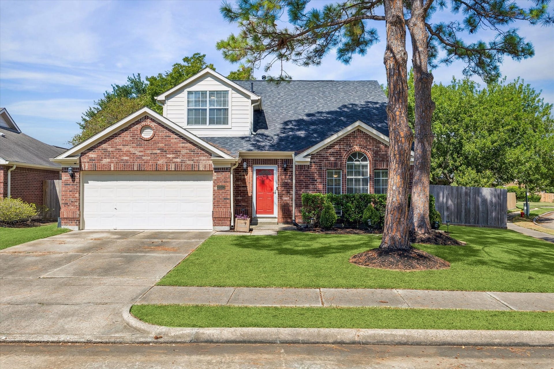 1043 Danforth Drive, Houston, TX 77062 Charming brick home with a welcoming red front door, two-car garage, and lush green lawn, accented by mature trees and manicured landscaping.