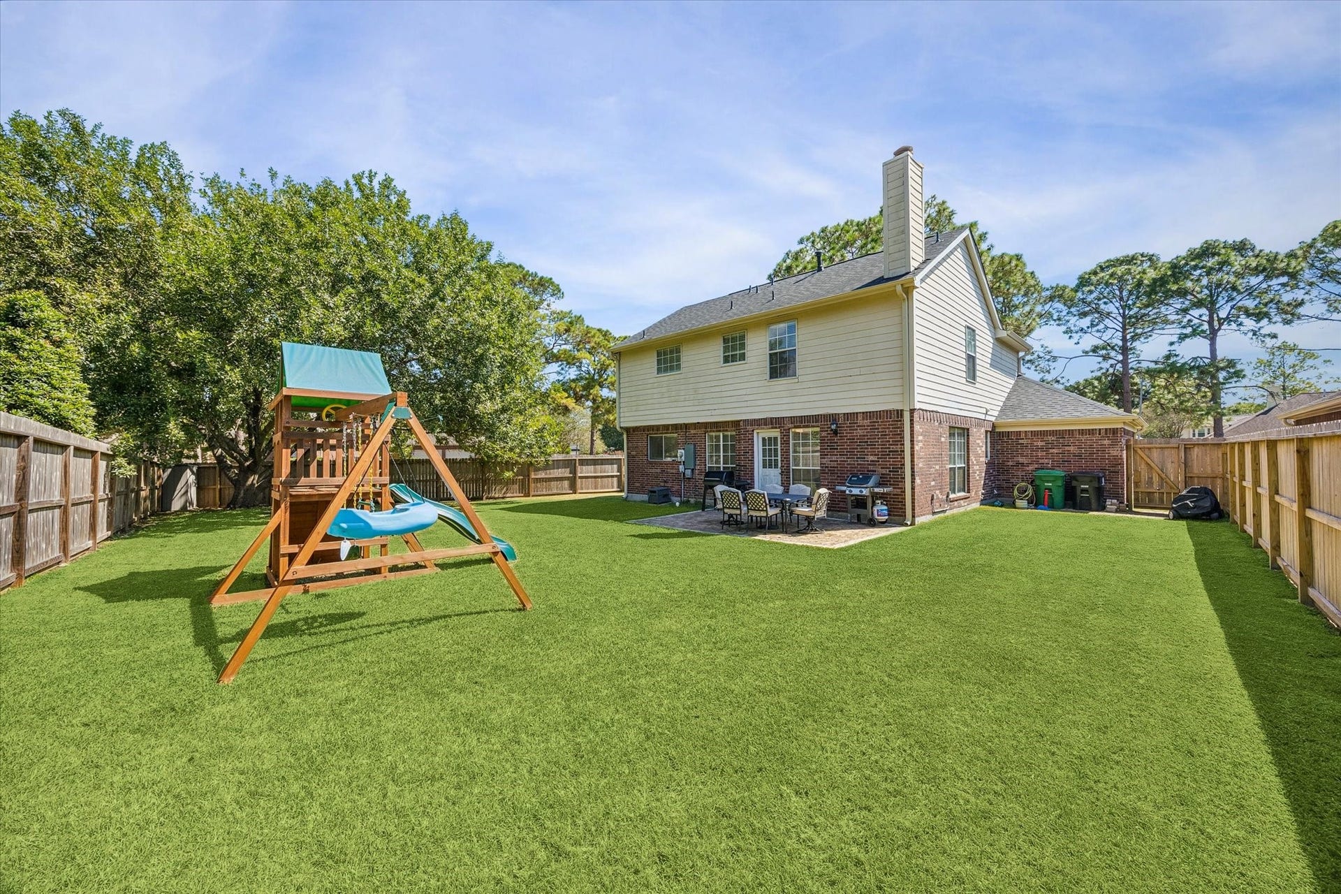 1043 Danforth Drive, Houston, TX 77062 Spacious backyard with lush green lawn, playset, and patio area perfect for outdoor entertaining and family fun.