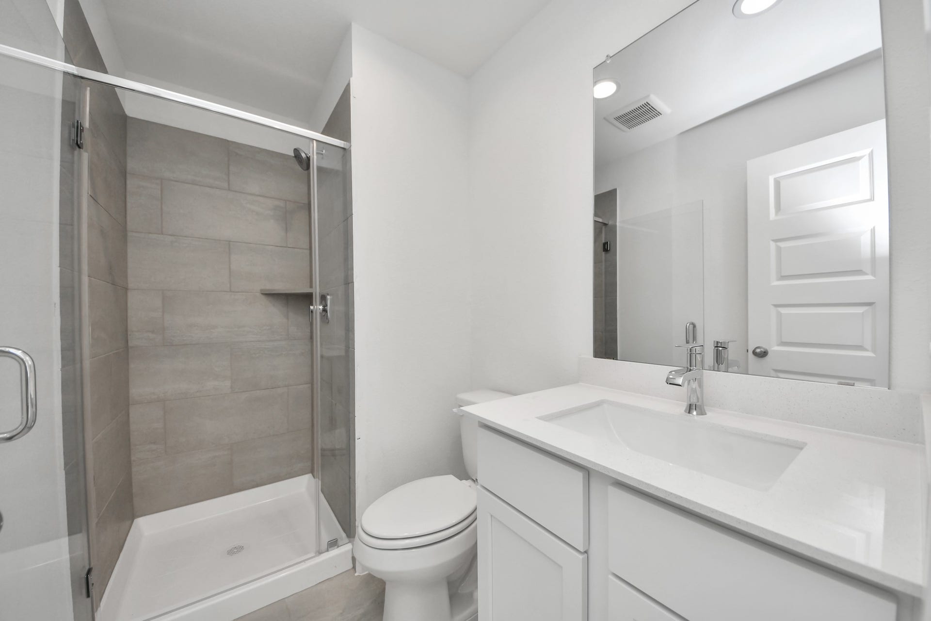 Secondary bath features tile flooring, walk-in shower with tile surround, light stained wood cabinets, beautiful light countertop. Sample photo of completed home with similar floor plan. Actual colors and selections may vary.