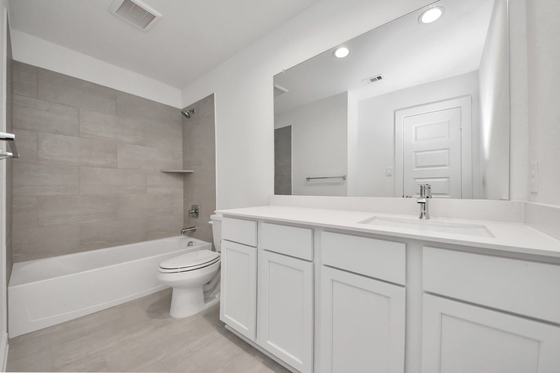 Secondary bath features tile flooring, bath/shower combo with tile surround, light stained wood cabinets, beautiful light countertop. Sample photo of completed home with similar floor plan. Actual colors and selections may vary.