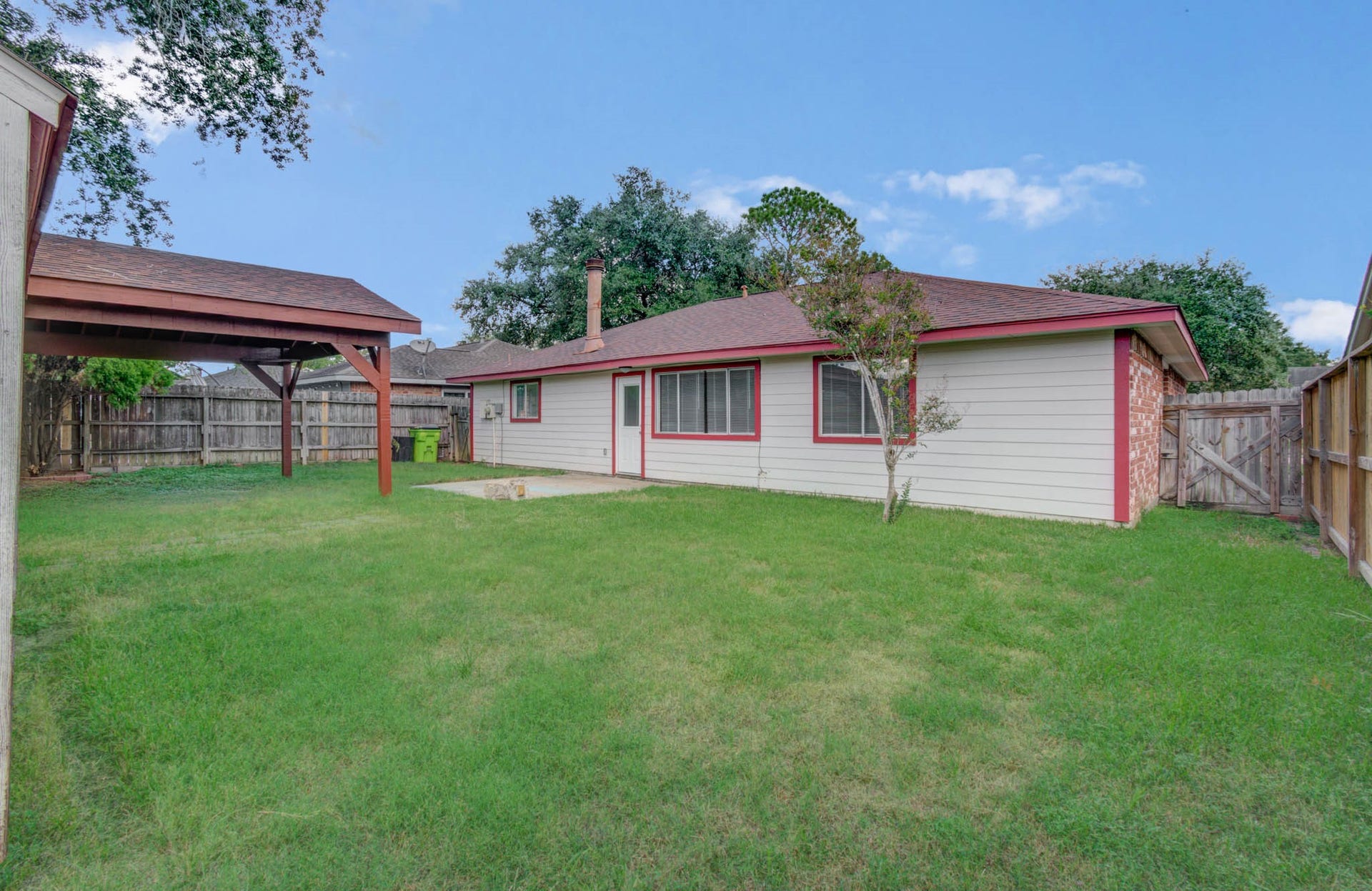 7319 Skybright Lane, Houston, TX 77095 Spacious backyard featuring a well-maintained lawn, a cozy single-story home with red trim, and a covered patio perfect for outdoor relaxation.