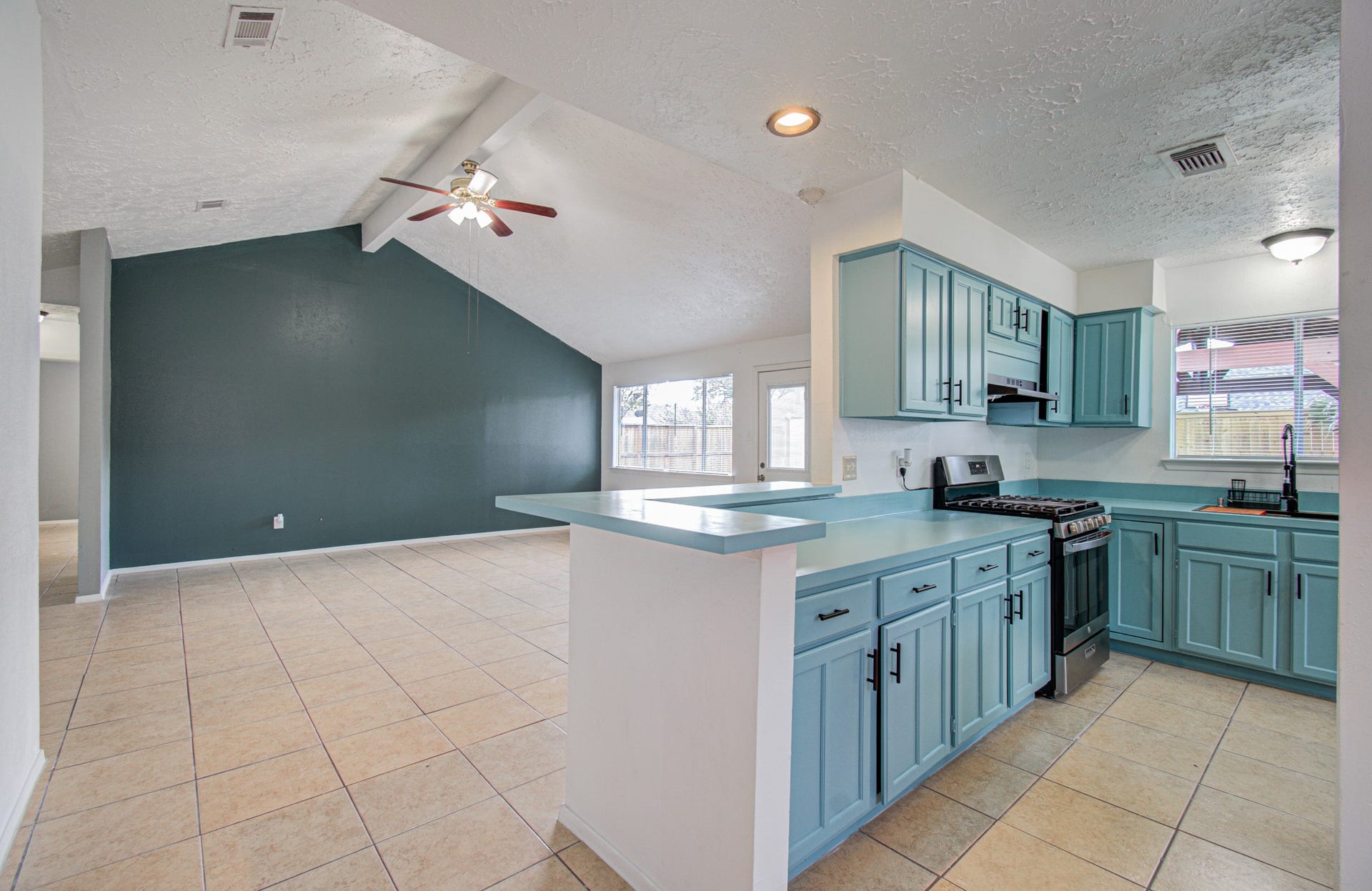 7319 Skybright Lane, Houston, TX 77095 Spacious open-concept living area featuring a modern kitchen with stylish teal cabinetry, stainless steel appliances, and ample natural light from large windows and a sliding door leading to the backyard.