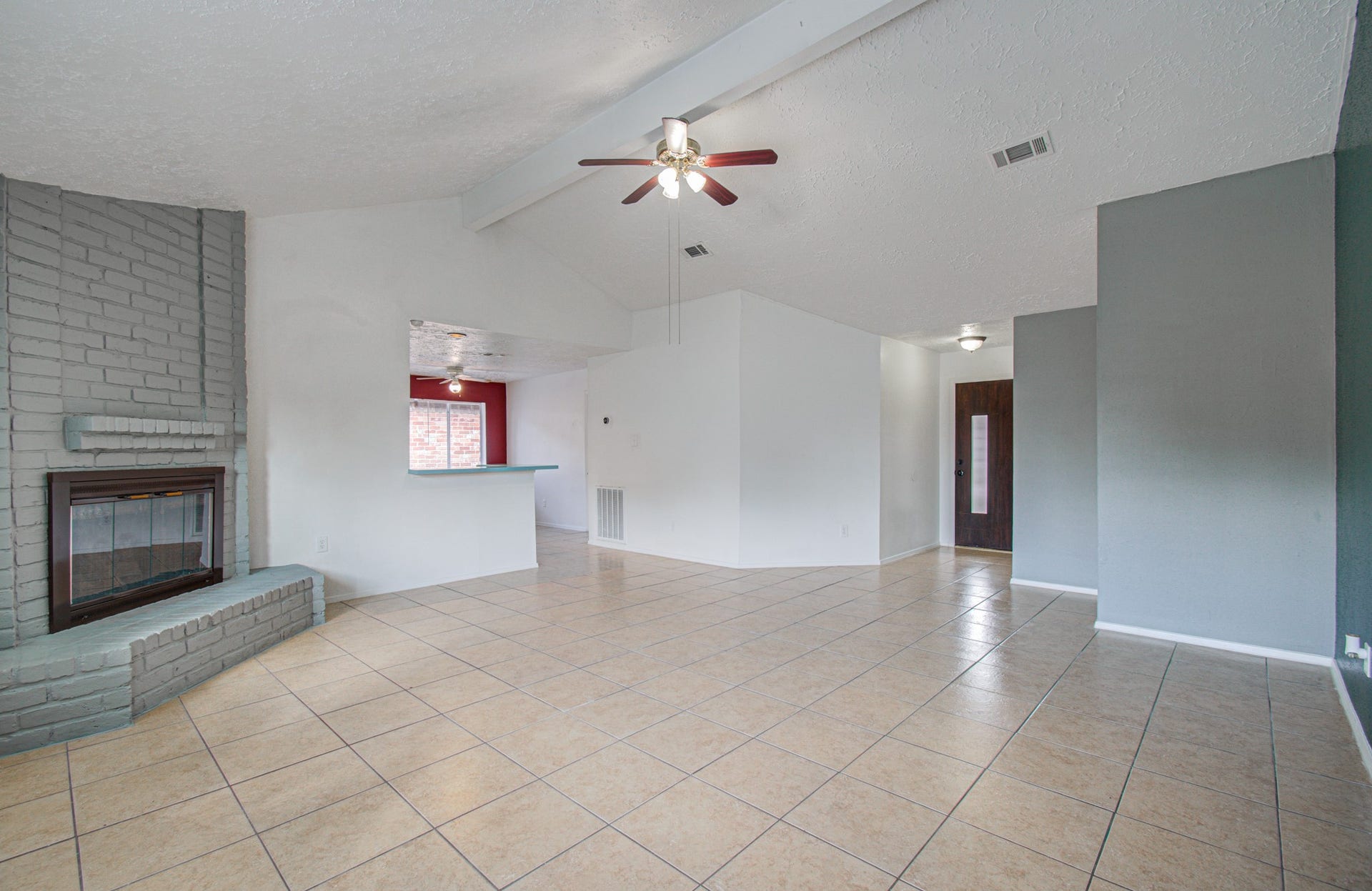 7319 Skybright Lane, Houston, TX 77095 Spacious living area with high ceilings, featuring a cozy brick fireplace and modern ceiling fan, complemented by neutral tile flooring and a pass-through to the kitchen.