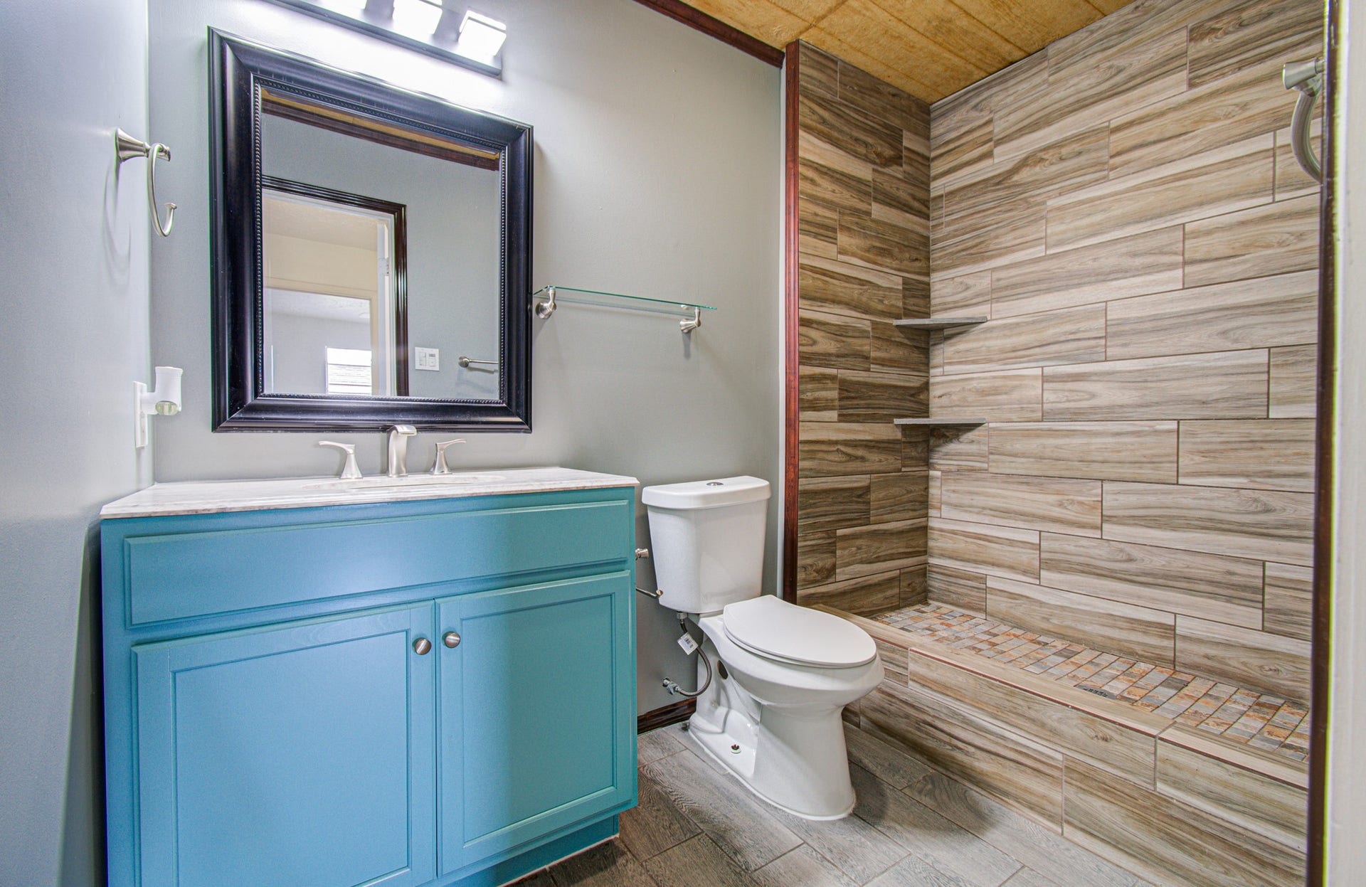 7319 Skybright Lane, Houston, TX 77095 Elegant bathroom featuring a striking wood-look tile shower, sleek blue vanity with modern fixtures, and a large framed mirror.