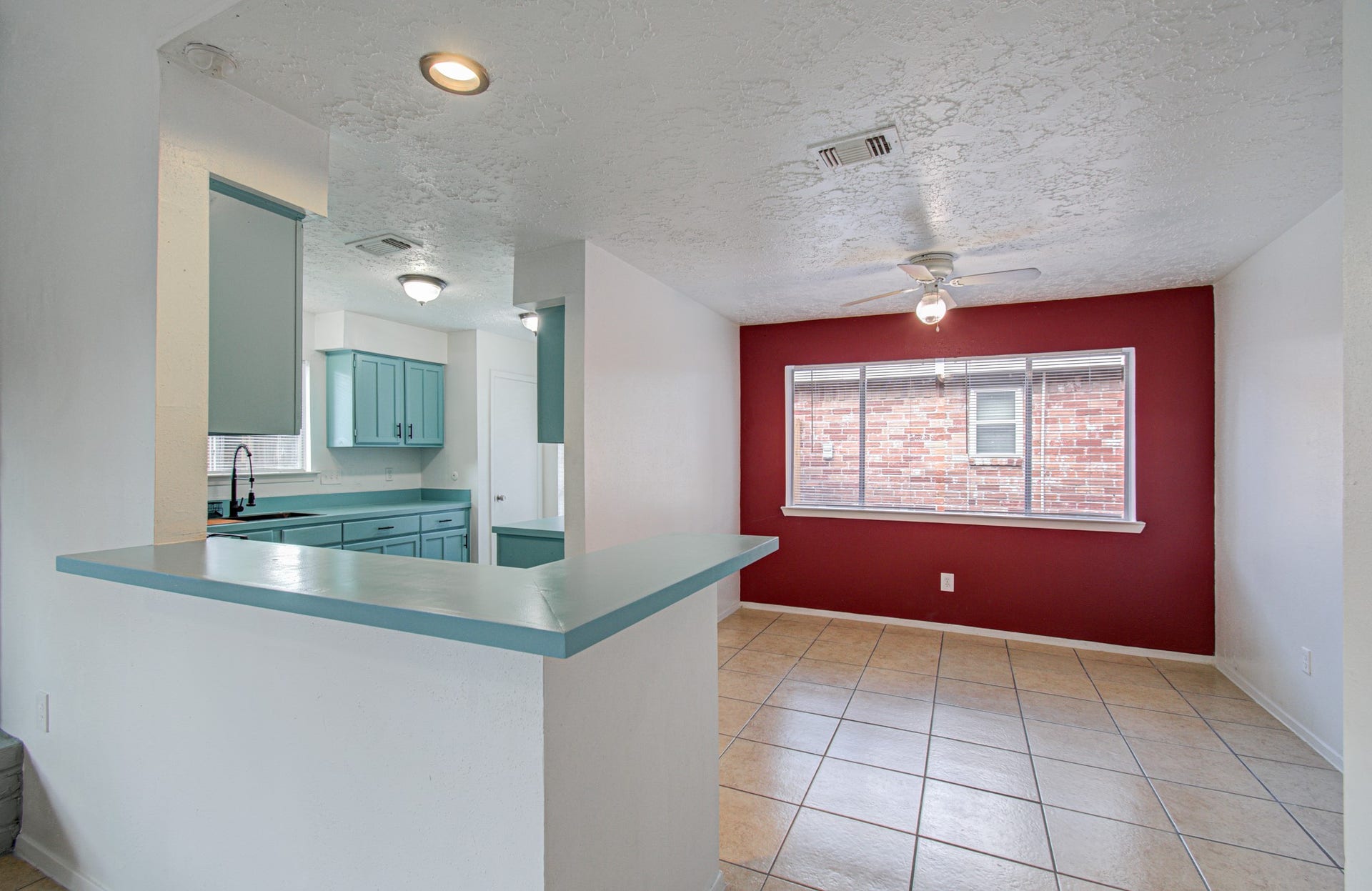 7319 Skybright Lane, Houston, TX 77095 Bright and inviting kitchen and dining area featuring teal cabinetry, a breakfast bar, and a bold accent wall, complemented by tile flooring and ample natural light.