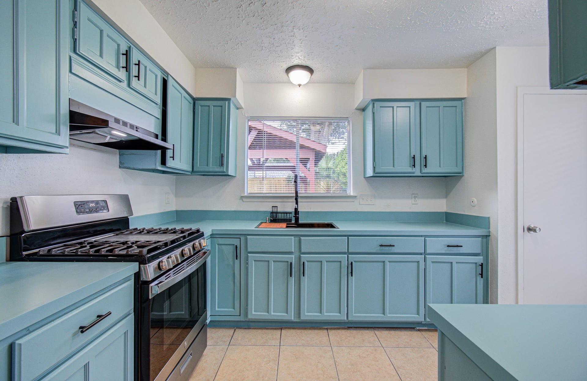 7319 Skybright Lane, Houston, TX 77095 Charming kitchen featuring stylish teal cabinetry, modern stainless steel appliances, and ample workspace, complemented by natural light from the window.