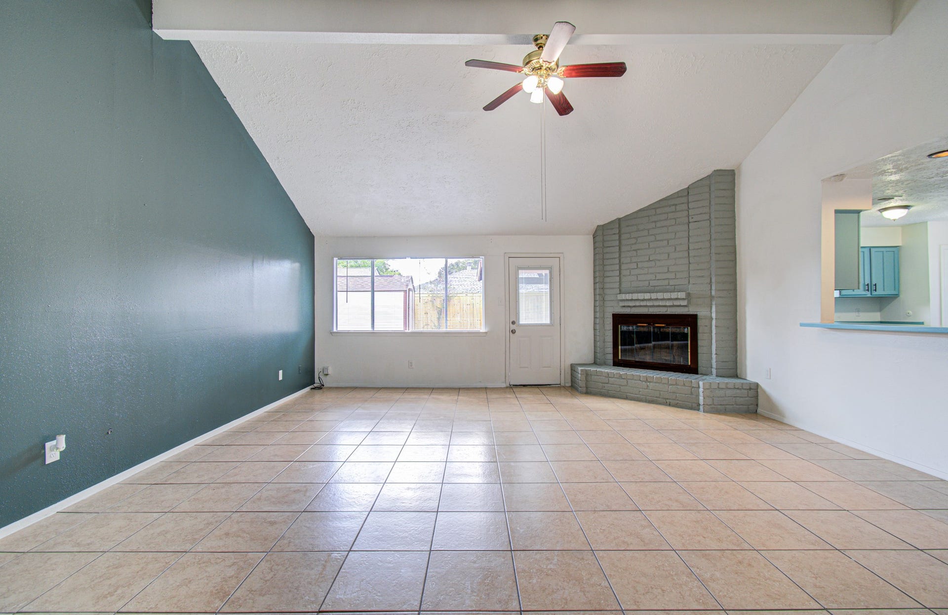 7319 Skybright Lane, Houston, TX 77095 Spacious living room with vaulted ceilings, a cozy brick fireplace, and plenty of natural light from large windows, complemented by a modern ceiling fan and open access to the kitchen.