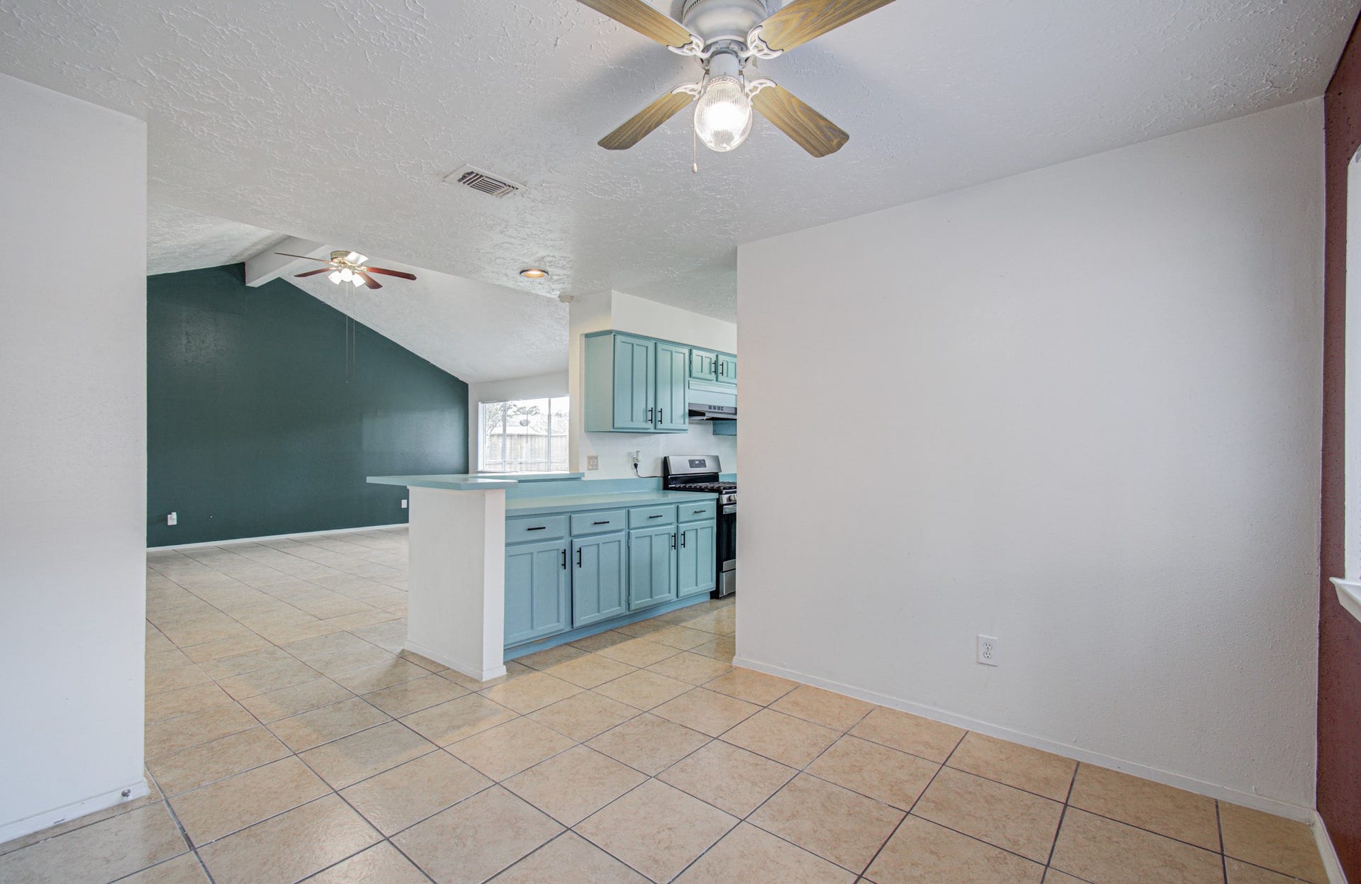 7319 Skybright Lane, Houston, TX 77095 Spacious open-concept kitchen and living area with tile flooring, vaulted ceiling, and modern teal cabinetry, perfect for entertaining.