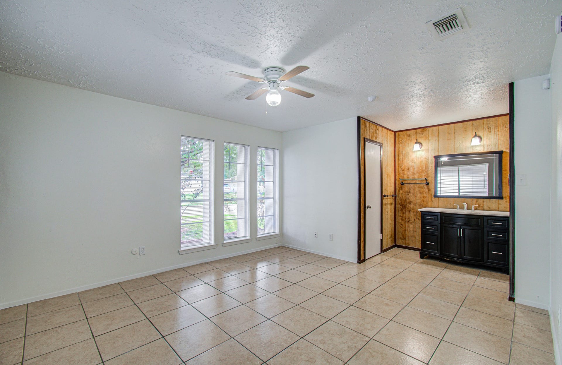 7319 Skybright Lane, Houston, TX 77095 Bright living space with large windows, tiled floors, and a ceiling fan, featuring a cozy corner with a modern vanity and wood accent wall.