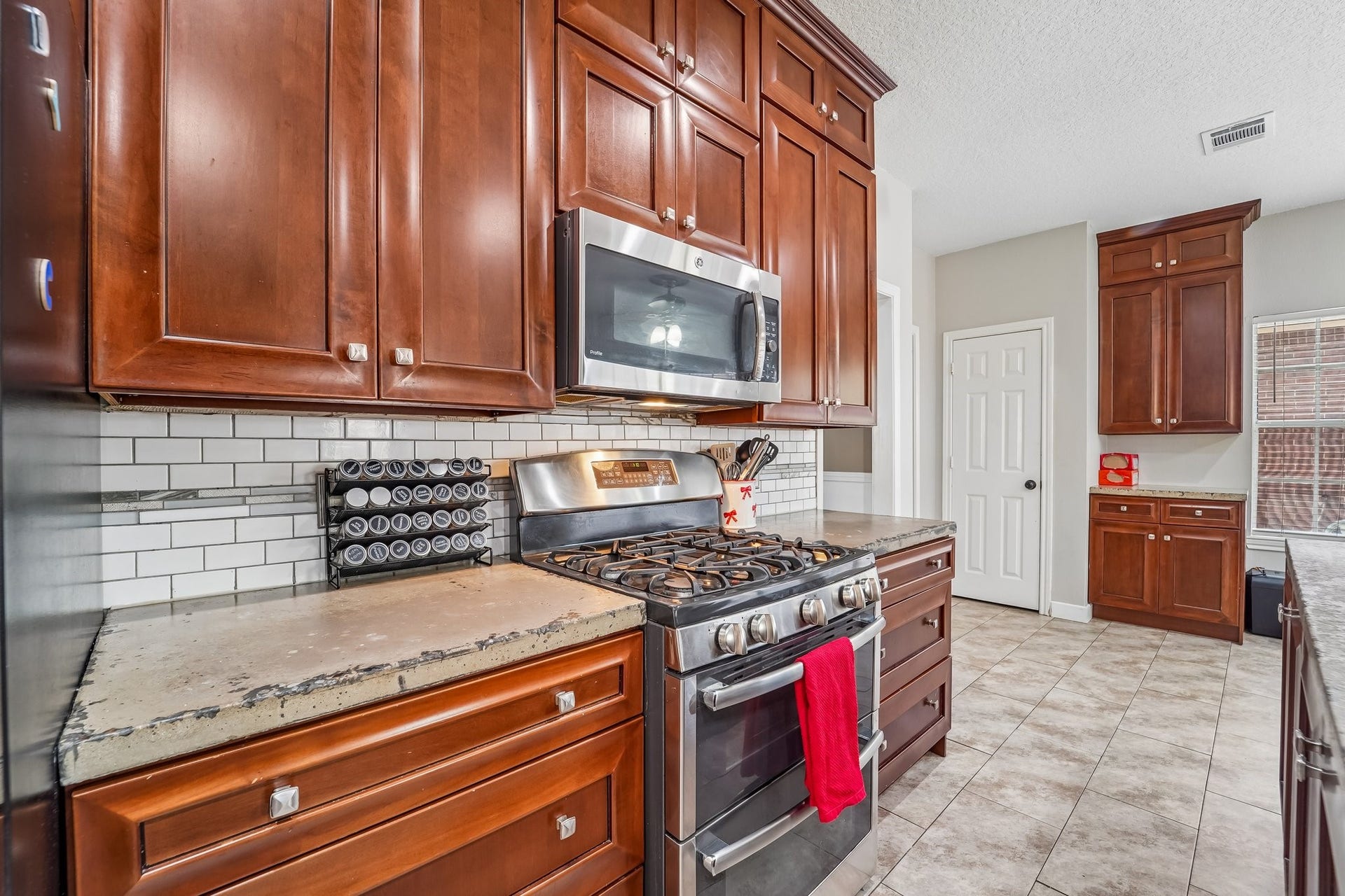 Elegant kitchen with rich wood cabinets, stainless steel appliances, and a stylish subway tile backsplash, complemented by durable tile flooring.