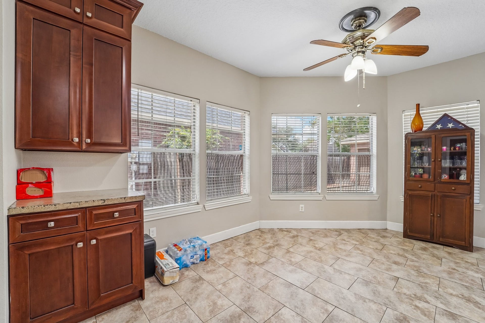 Bright and inviting space with large windows, elegant tile flooring, and rich wood cabinetry, perfect for dining or casual gatherings.