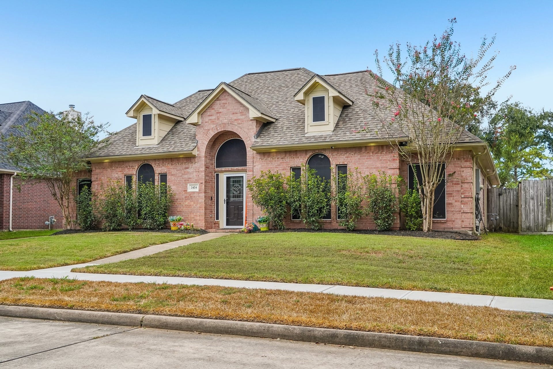 Charming brick home with a welcoming front entrance, arched windows, and lush landscaping, set on a well-maintained lawn.