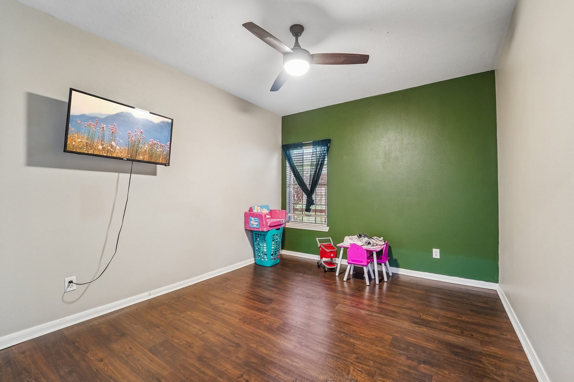 Spacious room with hardwood floors, a ceiling fan, and a large green accent wall, perfect for versatile use.