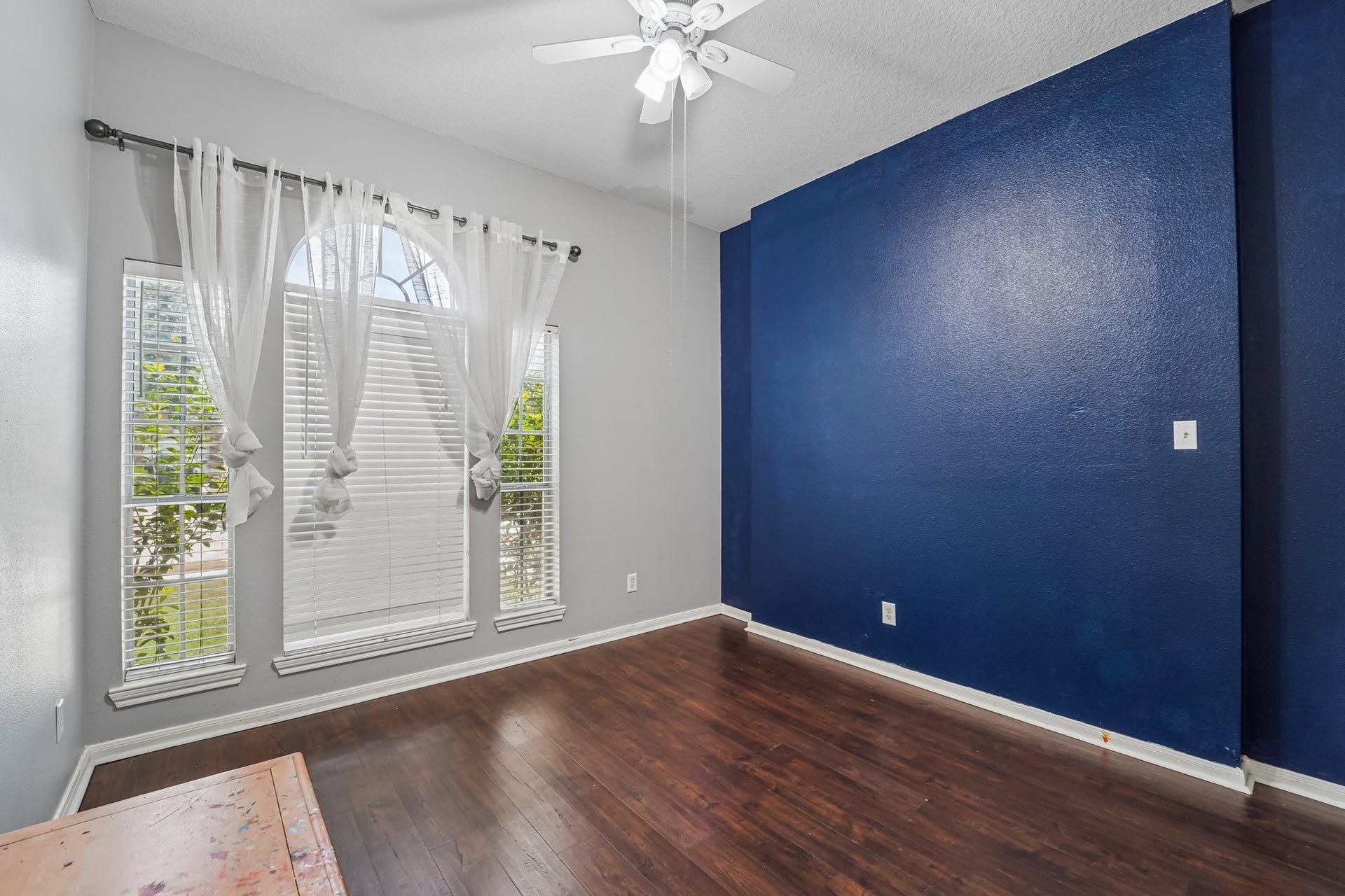 Bright and inviting room with rich hardwood floors, a striking deep blue accent wall, and large arched windows that fill the space with natural light.