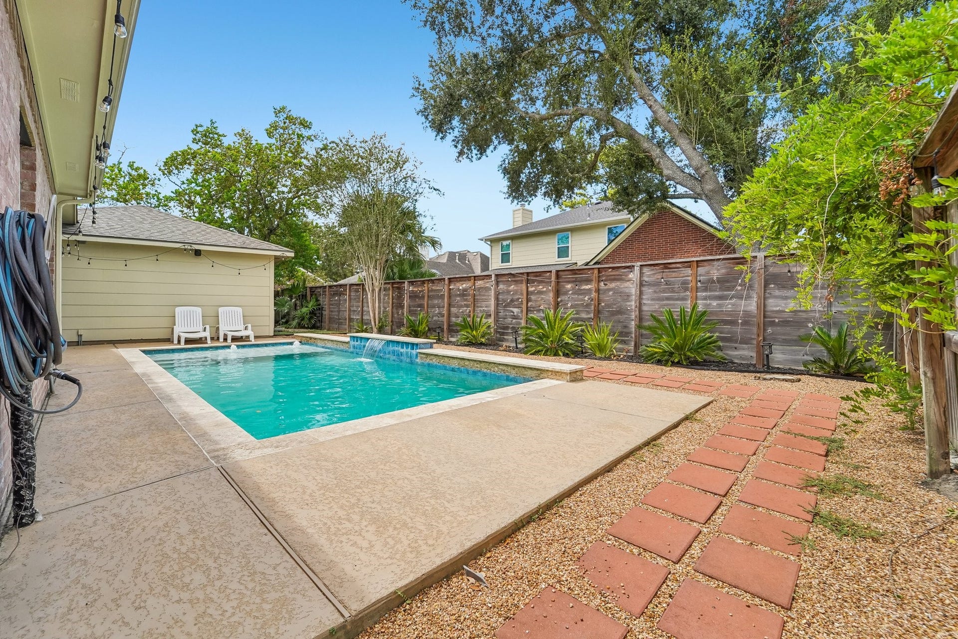 Enjoy a serene backyard oasis with a sparkling pool, surrounded by lush greenery and a privacy fence, perfect for relaxation and entertainment.