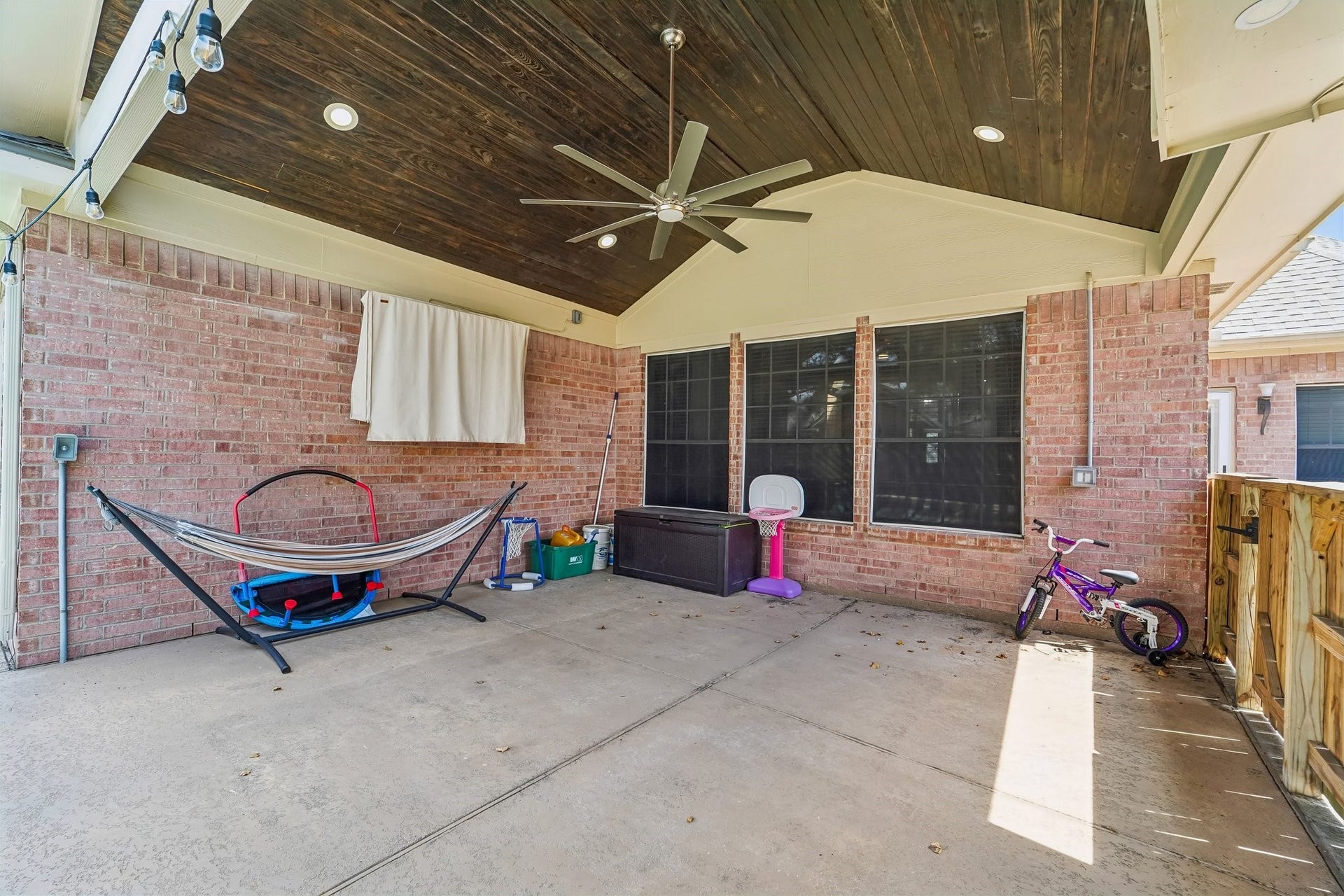 Spacious covered patio with a vaulted ceiling, perfect for outdoor entertaining, complete with a ceiling fan for comfort and ample room for relaxation and play.