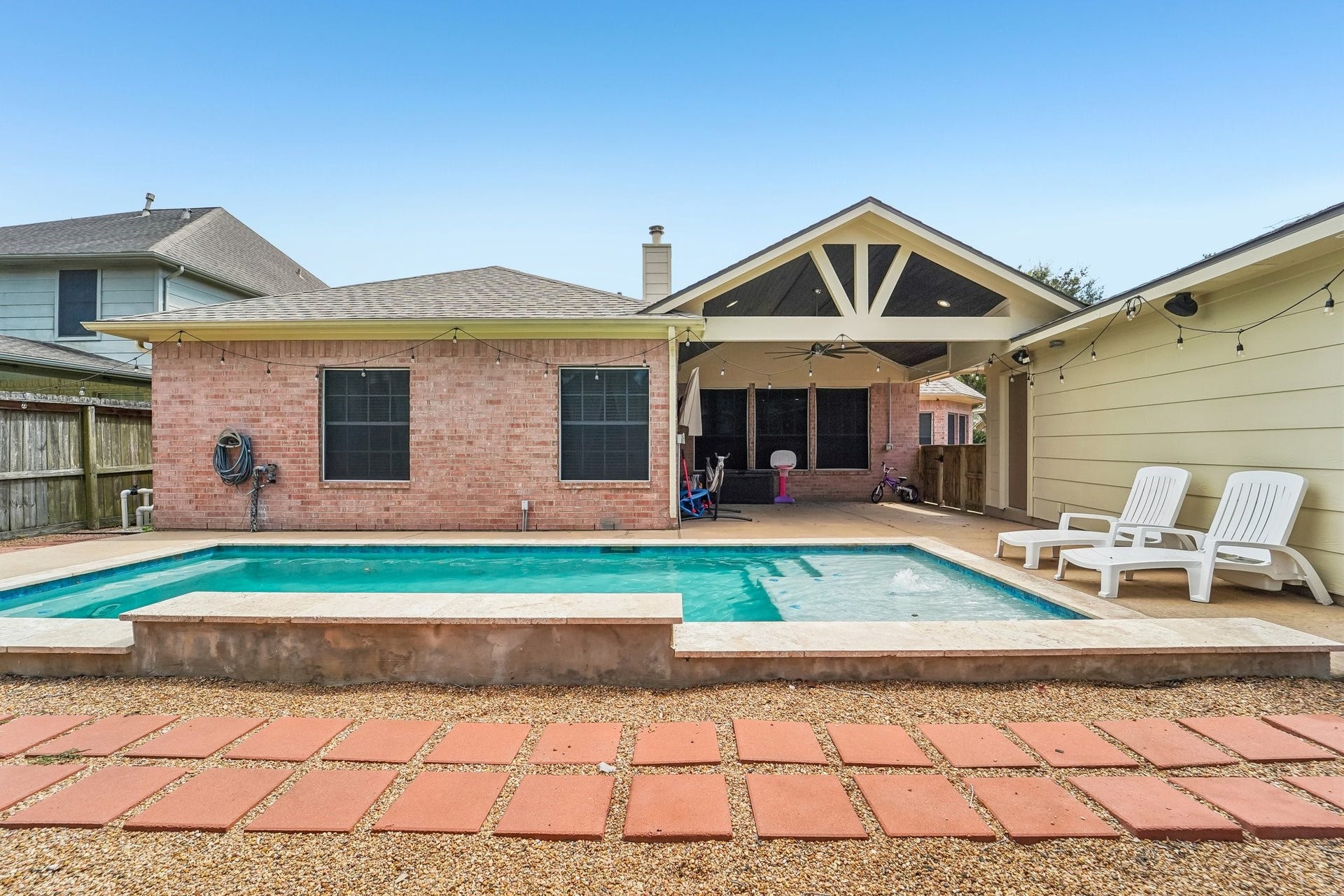 Charming backyard retreat featuring a sparkling pool, spacious patio, and cozy covered seating area perfect for outdoor relaxation and entertaining.
