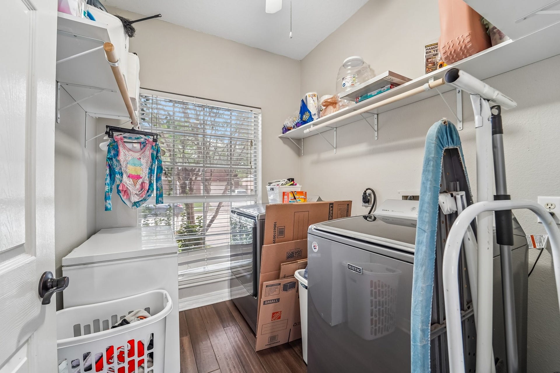 Bright laundry room with ample shelving, a window for natural light, and washer-dryer setup.